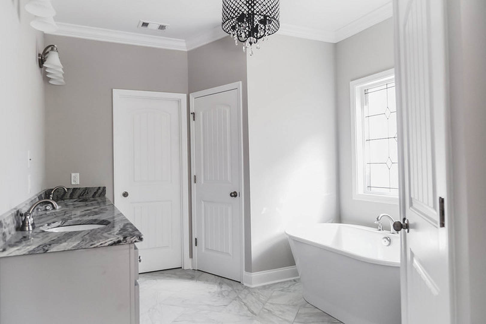 Marble countertop with undermount sink, white freestanding bathtub, light cabinetry, and neutral tile walls in a modern bathroom