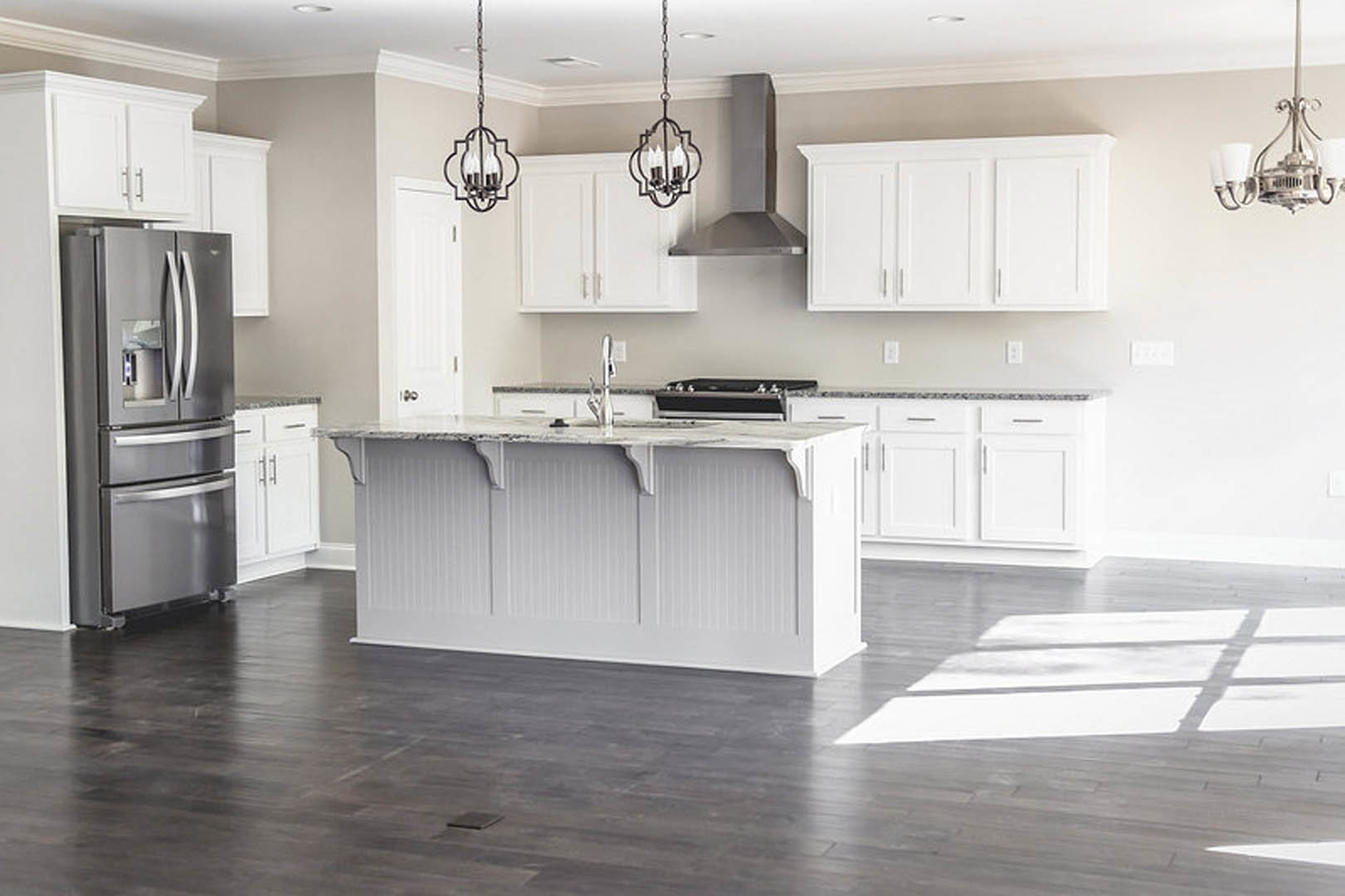 White kitchen with shaker cabinets, black stove, marble countertop, stainless refrigerator, pendant light fixture, and farmhouse sink