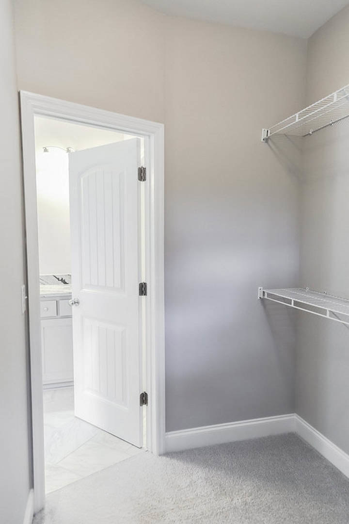 White paneled door with silver knobs, white wall-mounted shelf, plush white carpet, and smooth plaster walls in a bathroom interior.