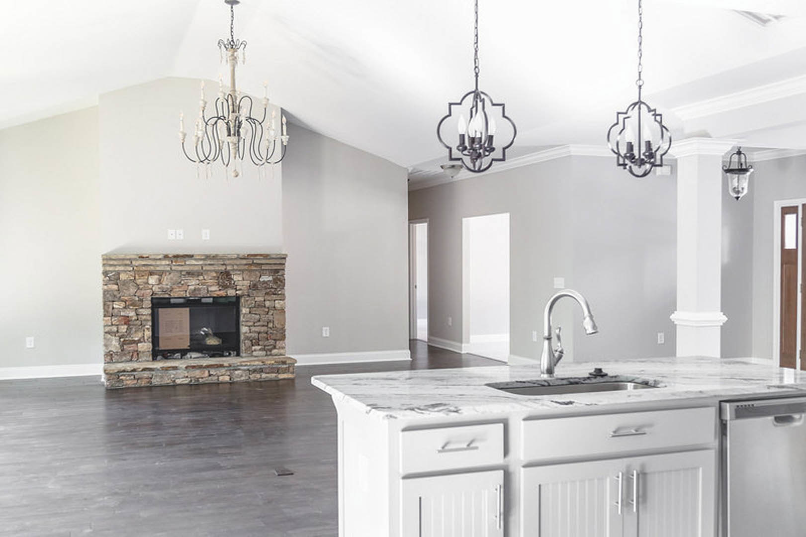 Open-concept kitchen featuring a stone fireplace with glass enclosure, white cabinetry, marble countertops, stainless steel sink and faucet, crystal chandelier, and large windows.