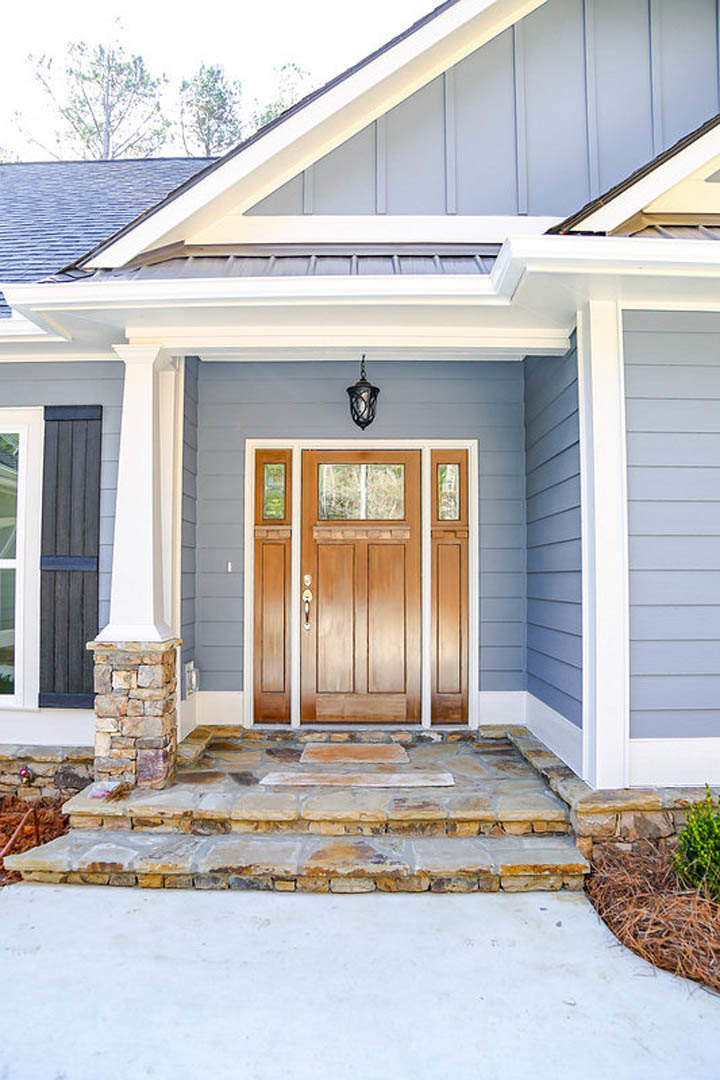 Dark wood front door with glass panels, stone steps leading to entry, white siding, and porch area visible