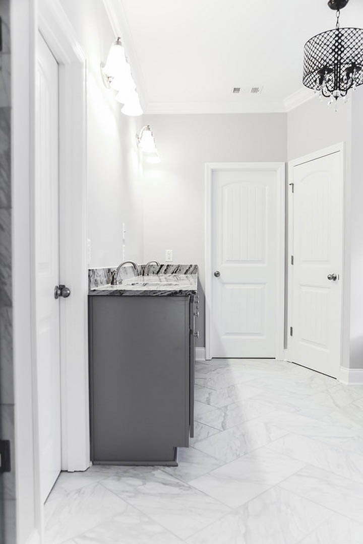 Bathroom with polished marble floor, white door with silver knobs, black vanity cabinet, and modern sink fixtures