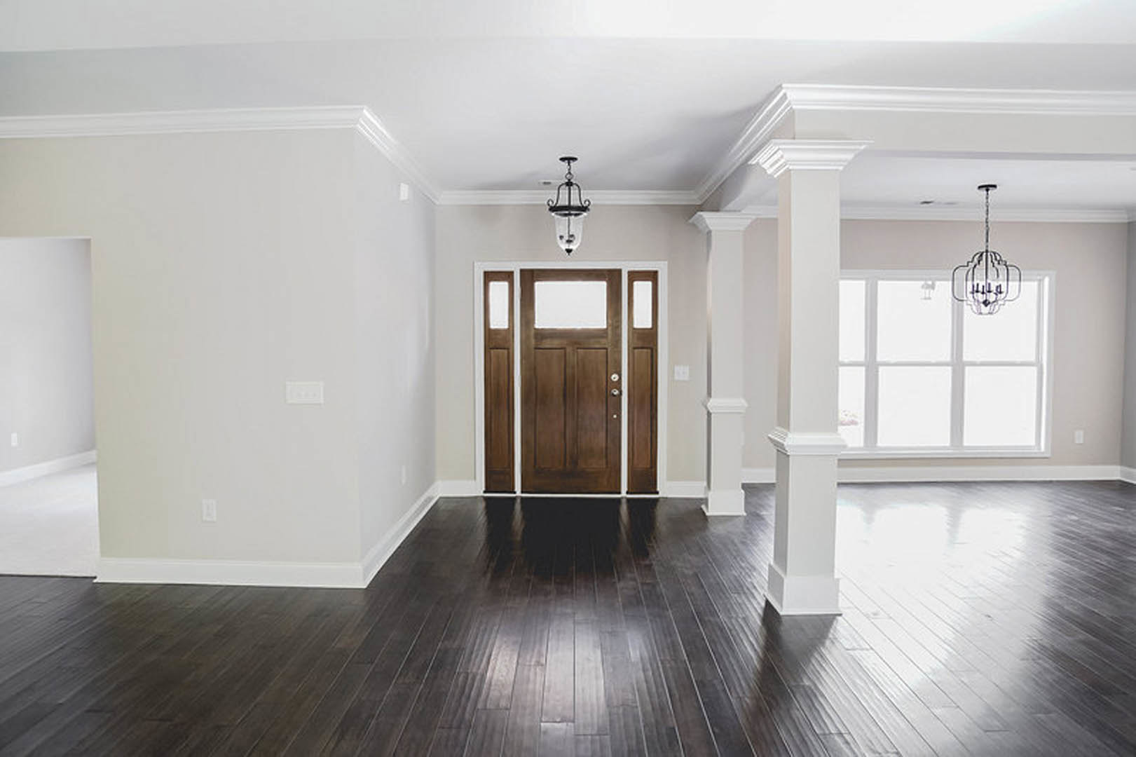 Dark wood flooring with white walls, a paneled door, and a modern black and white chandelier overhead.