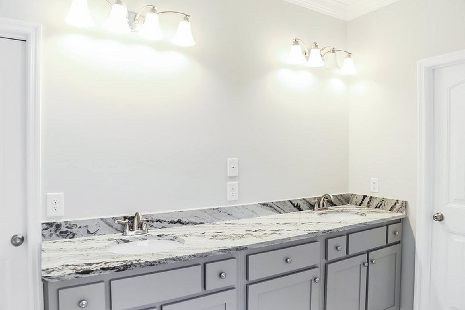 Bathroom featuring marble countertops, white cabinetry with drawers, white wall accented by a black stripe, modern light fixture, and silver faucet