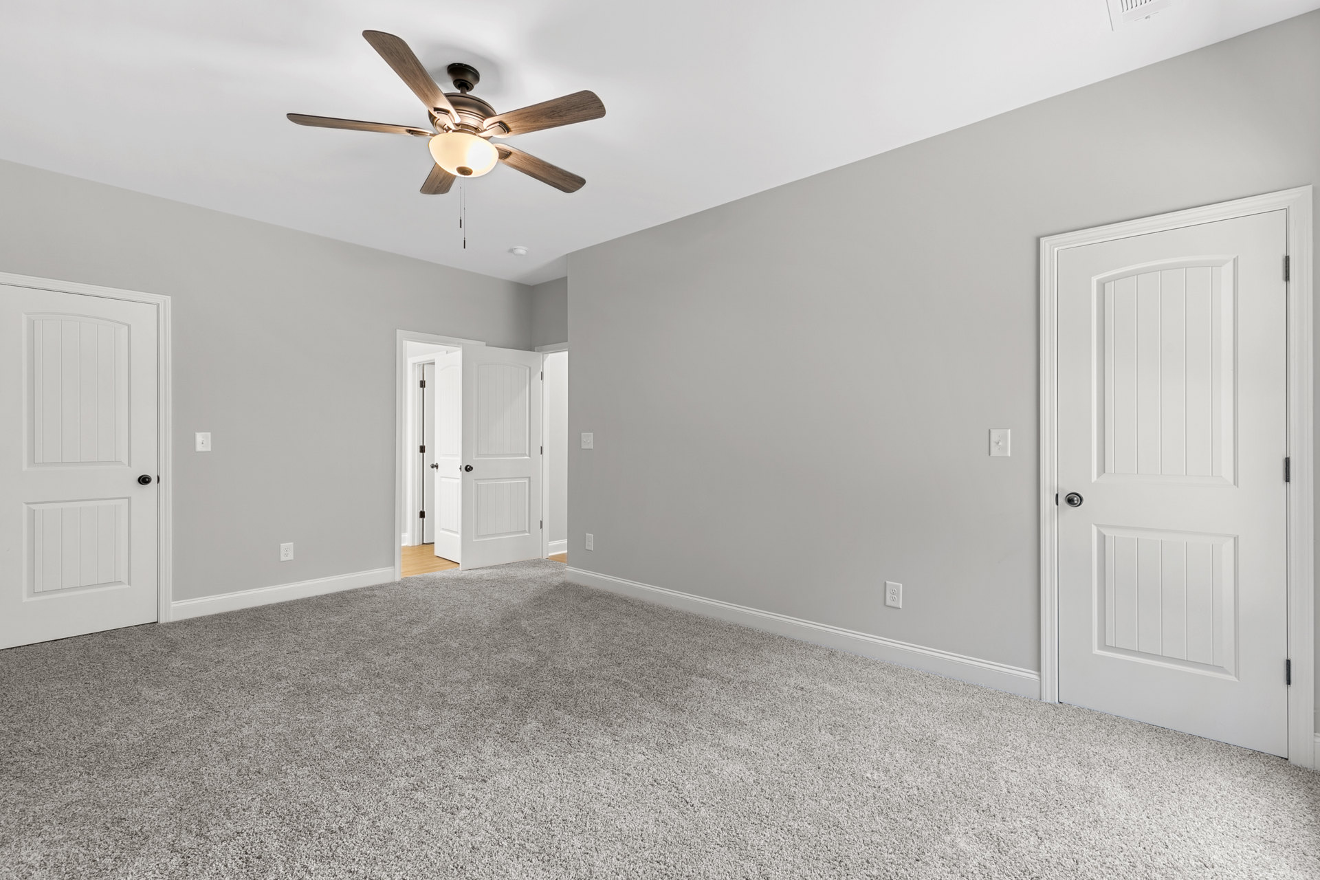 Ceiling fan with light fixture mounted above carpeted floor, white door with silver handle partially open, neutral walls with crown molding