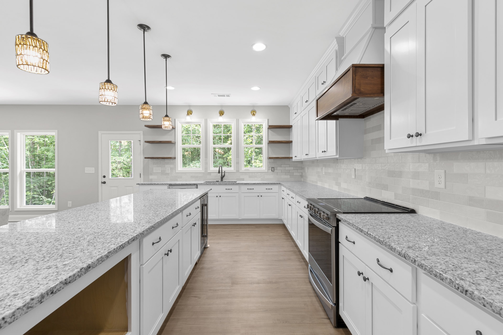 White kitchen cabinets, granite countertops, stainless steel sink, modern light fixture, window overlooking leafy trees