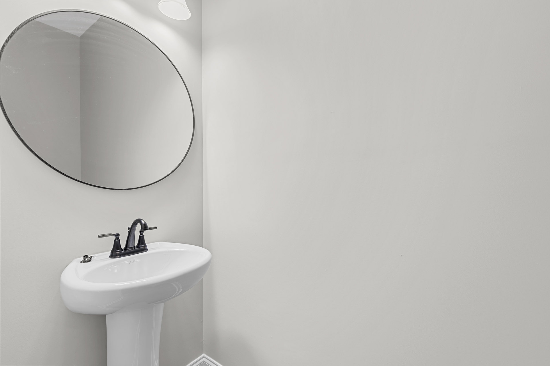 White pedestal sink with matte black faucet beneath circular wall-mounted mirror in modern bathroom