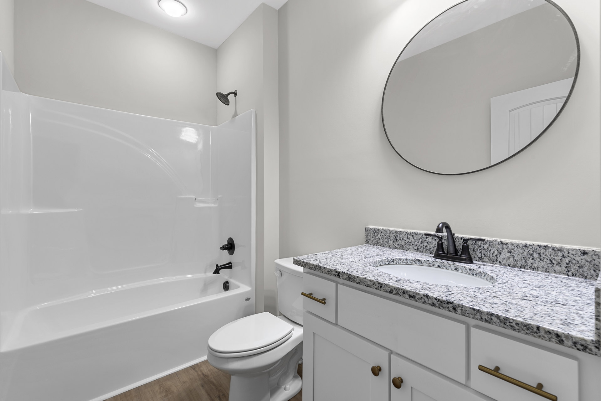 Modern bathroom featuring white tile walls, round mirror above a rectangular sink with chrome faucet, white toilet, and partial view of a bathtub.