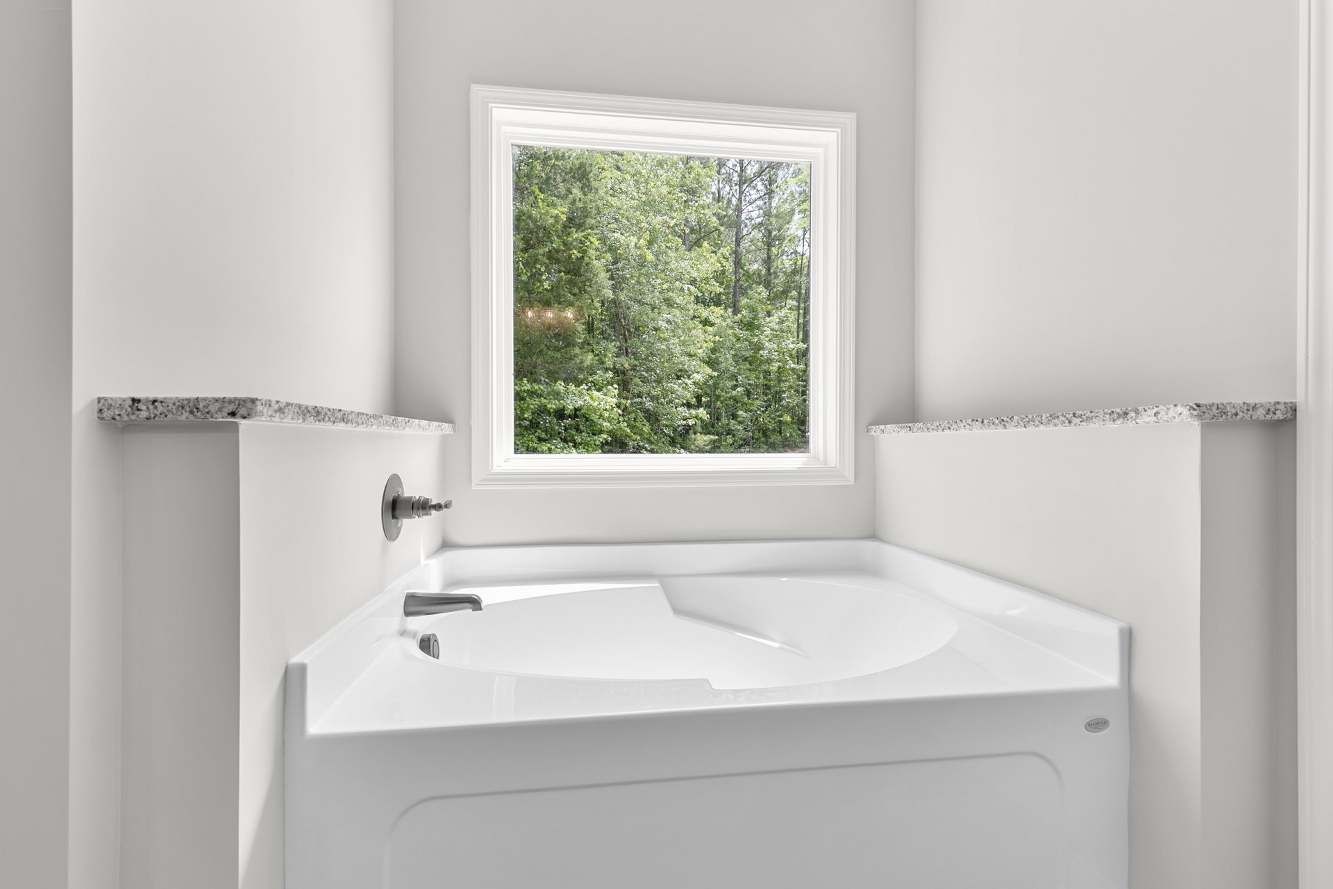 Freestanding white bathtub beneath a large window with tree views, white walls, chrome faucet, and minimal bathroom decor