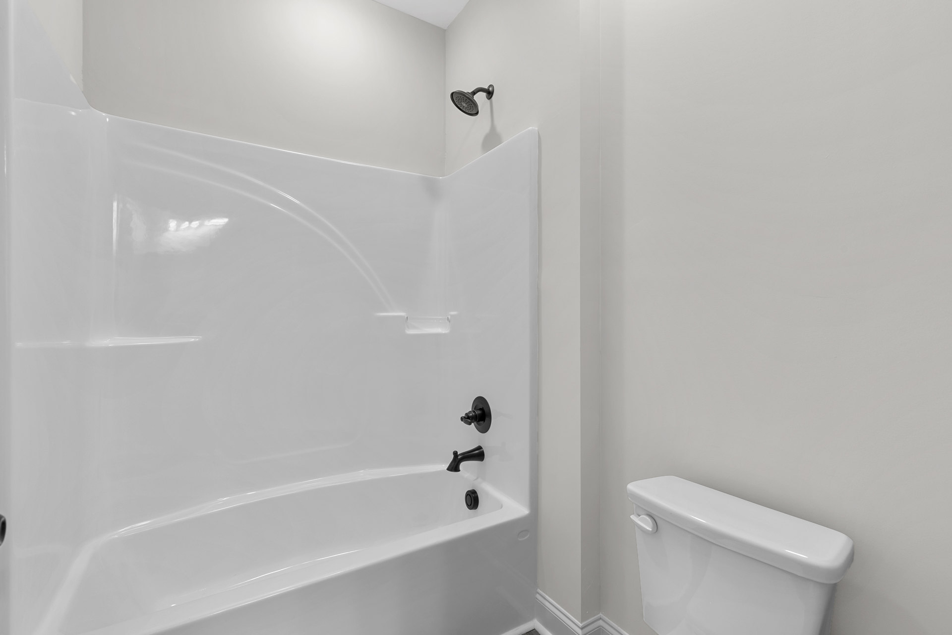 White bathtub with matte black faucet and fixtures, adjacent to a white toilet, set against smooth white tile walls in a modern bathroom.