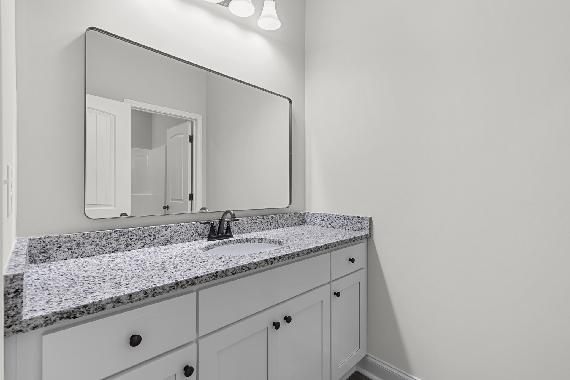 Marble countertop with undermount sink, chrome faucet, white cabinetry, large wall mirror, open door revealing tiled bathtub area