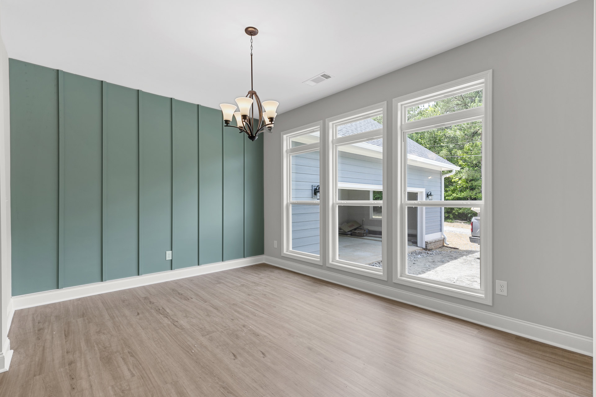 Chandelier with five lights hanging in a room featuring large windows, white walls, and wood flooring