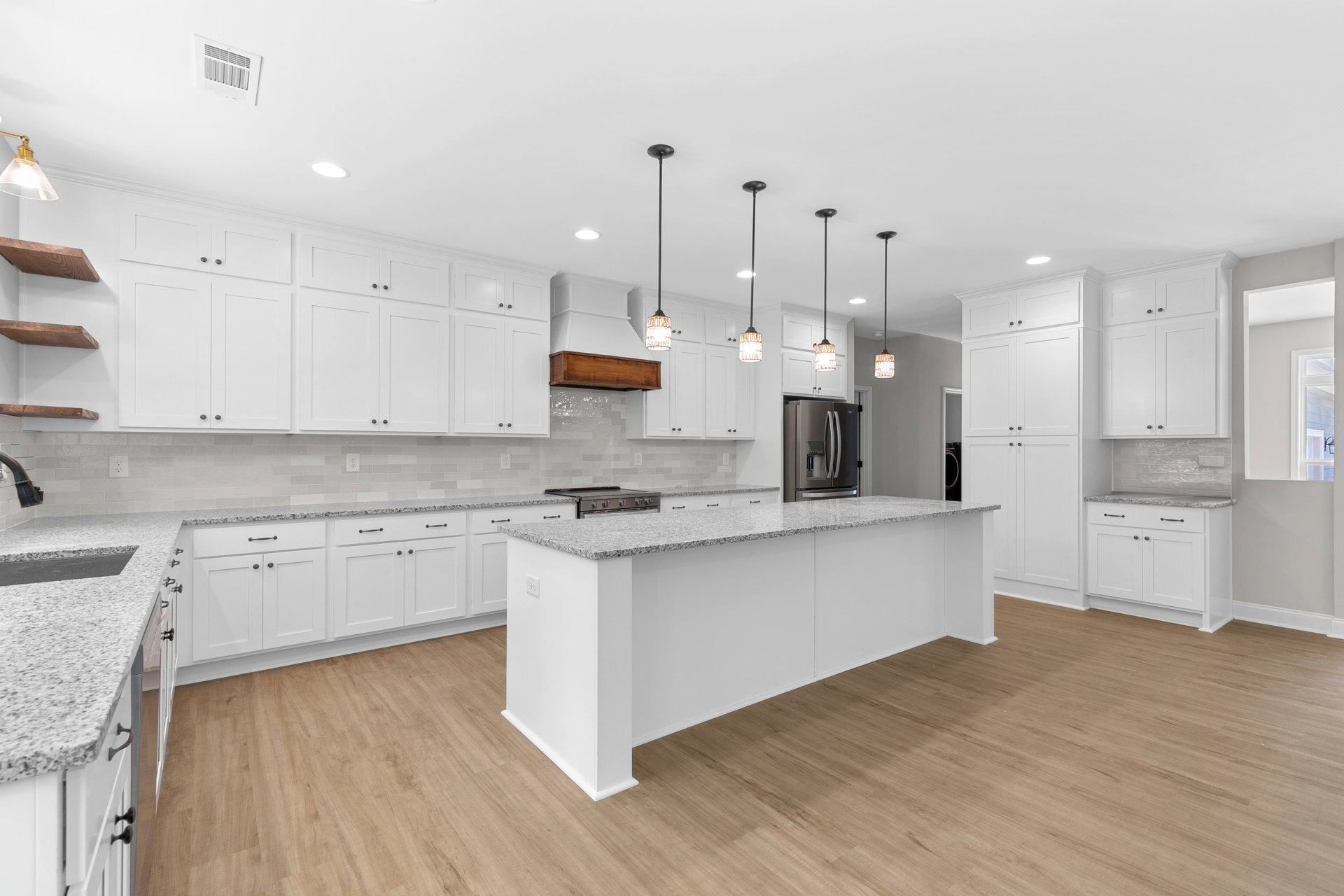 Kitchen with white shaker cabinets, marble countertop island, stainless steel refrigerator, wood plank flooring, clear glass pendant light, white walls