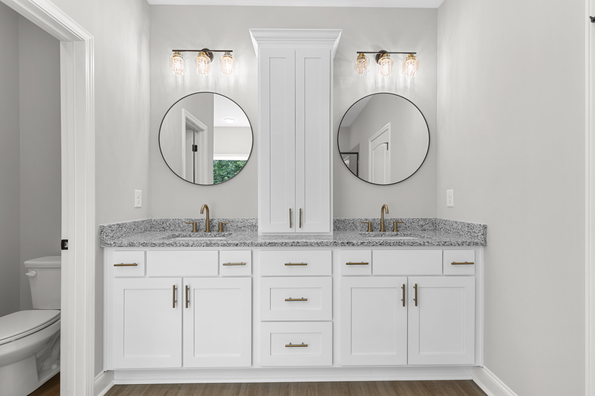 White bathroom cabinets with marble countertops, large wall mirror, chrome faucet, close-up of toilet, modern light fixture, white drawers with metal handles, tiled floor.