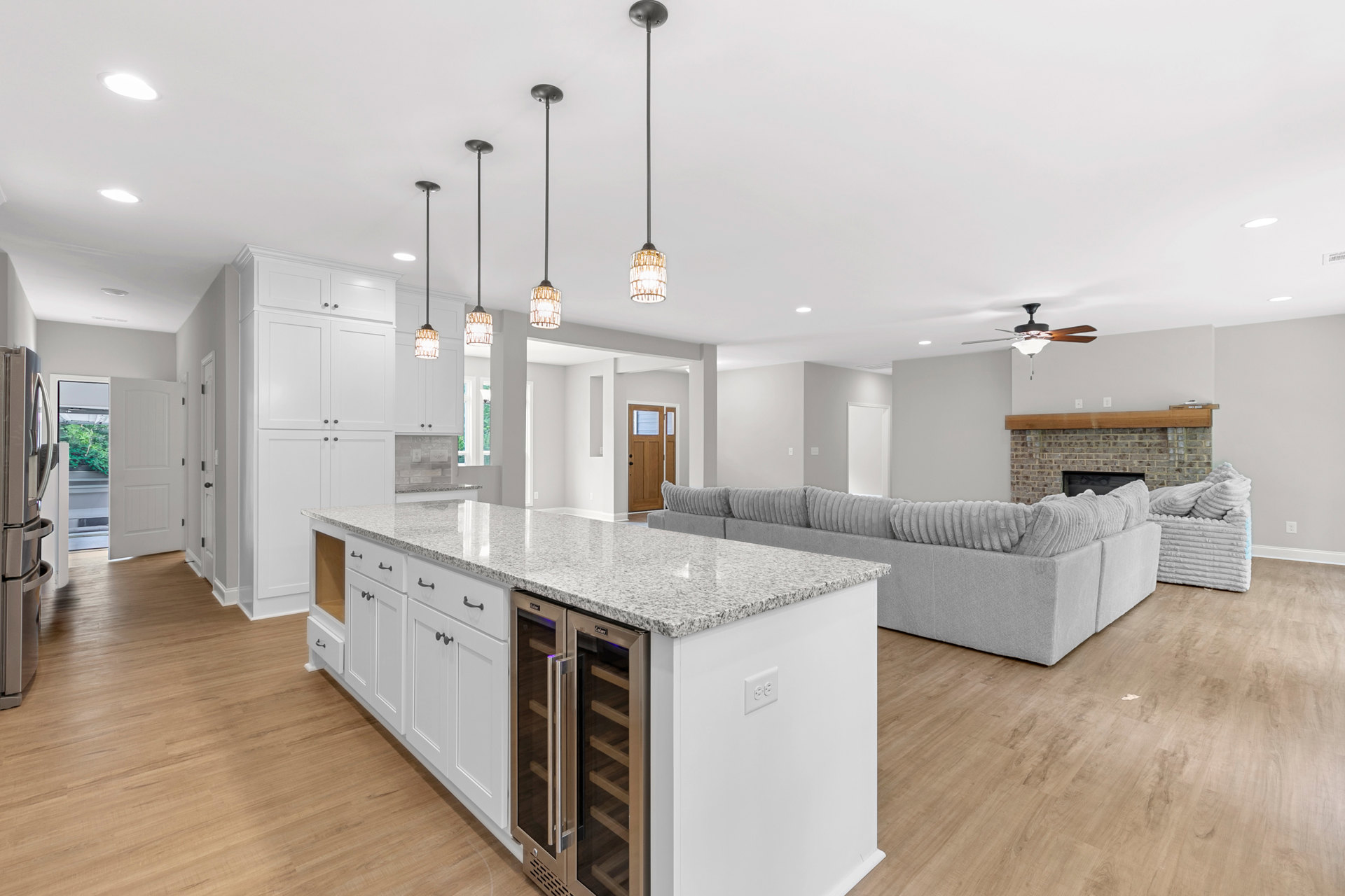 Open-concept kitchen and living room featuring a stainless steel refrigerator, granite countertops, white cabinetry, marble-topped island, built-in fireplace, light fixtures, and