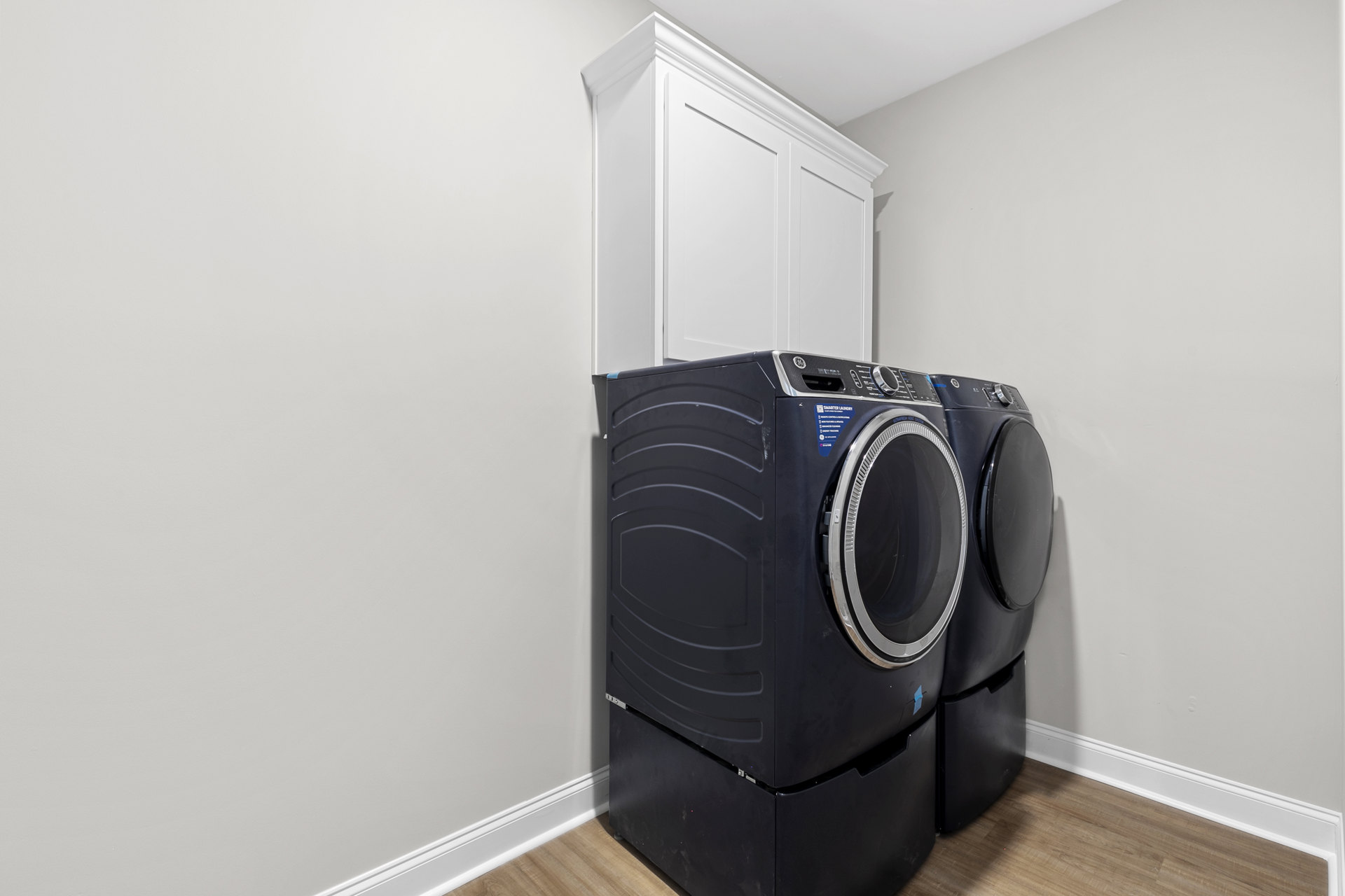 Front-loading washing machine and dryer set against white cabinetry in a laundry room with light walls and flooring