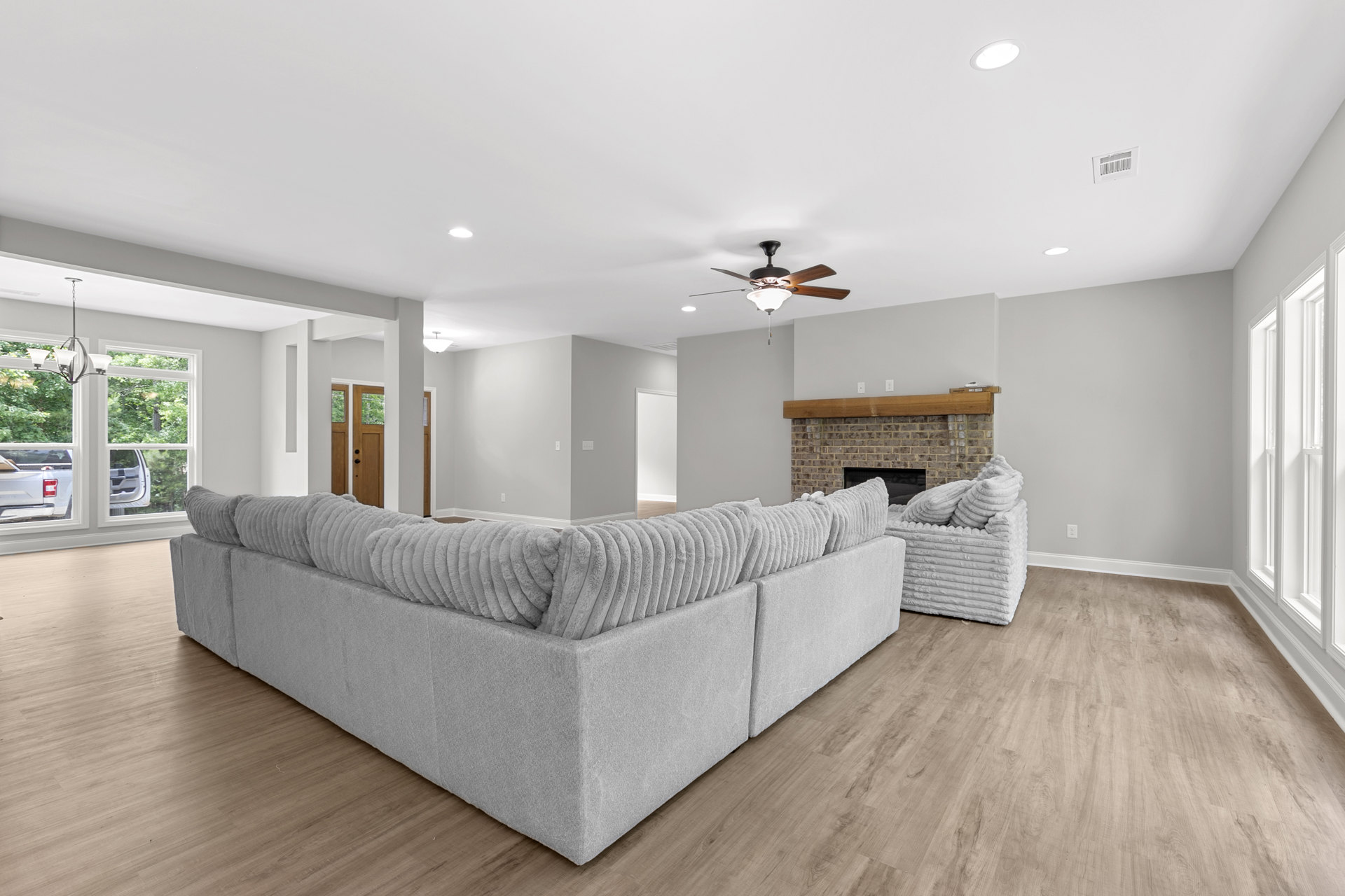Living room with white couch and pillows, stone fireplace, wood flooring, large window with view of white truck outside
