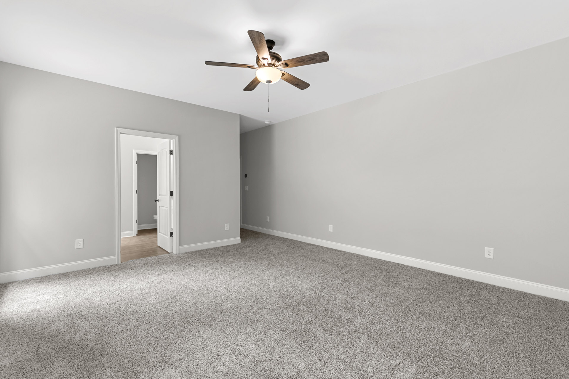 Carpeted bedroom with white walls, ceiling fan with light fixture, and adjacent bathroom visible through open white door