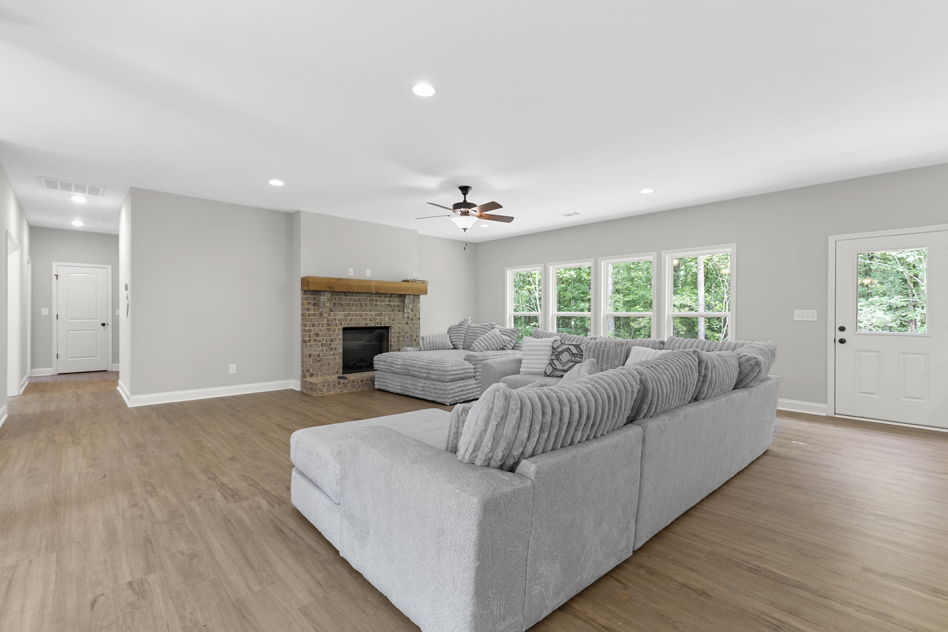 Spacious living room with a large sectional couch, wood flooring, white door with black knobs and window, fireplace topped with folded blankets, neutral walls