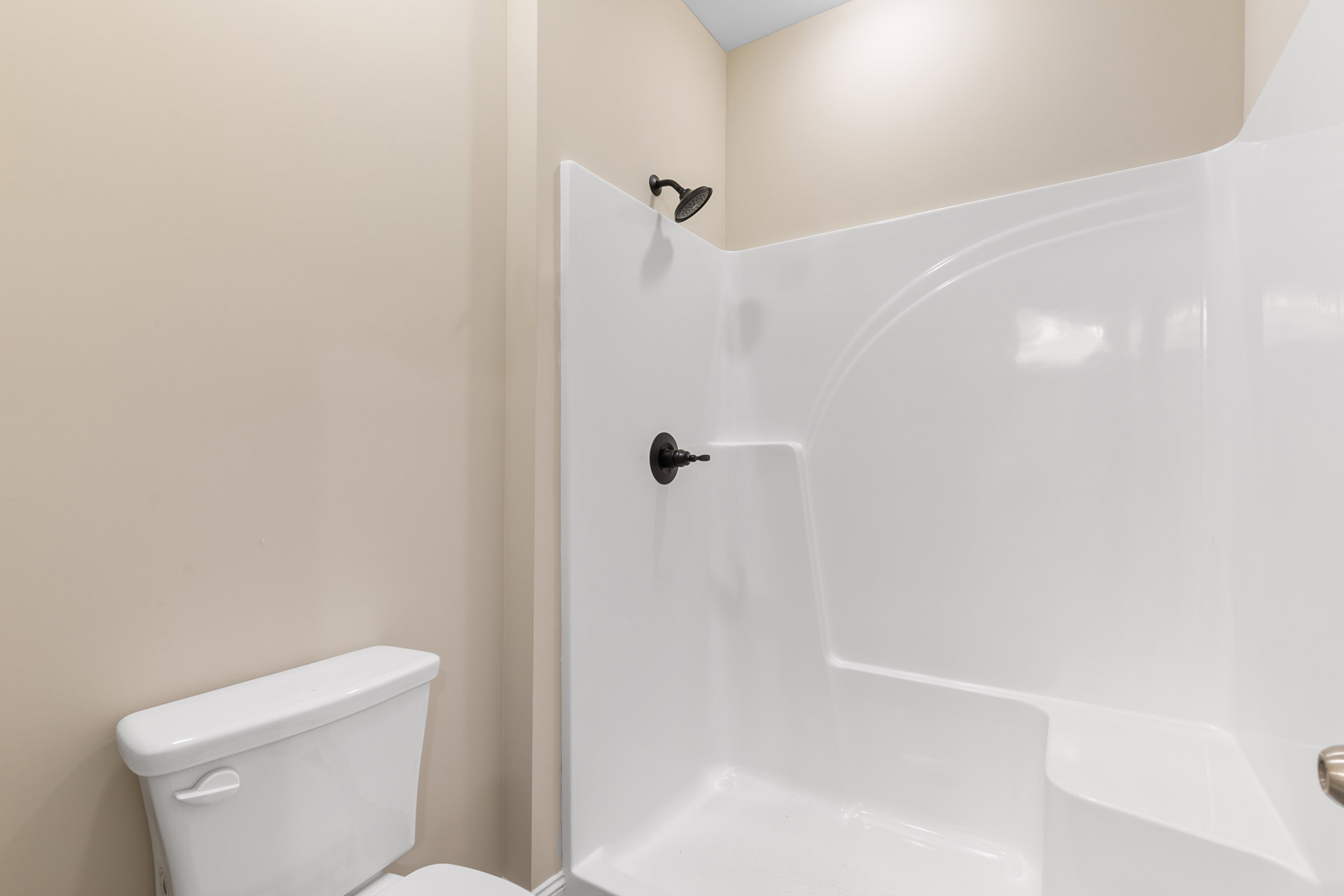White tile shower with black showerhead, white toilet with chrome handle, and partial view of white bathtub in modern bathroom.