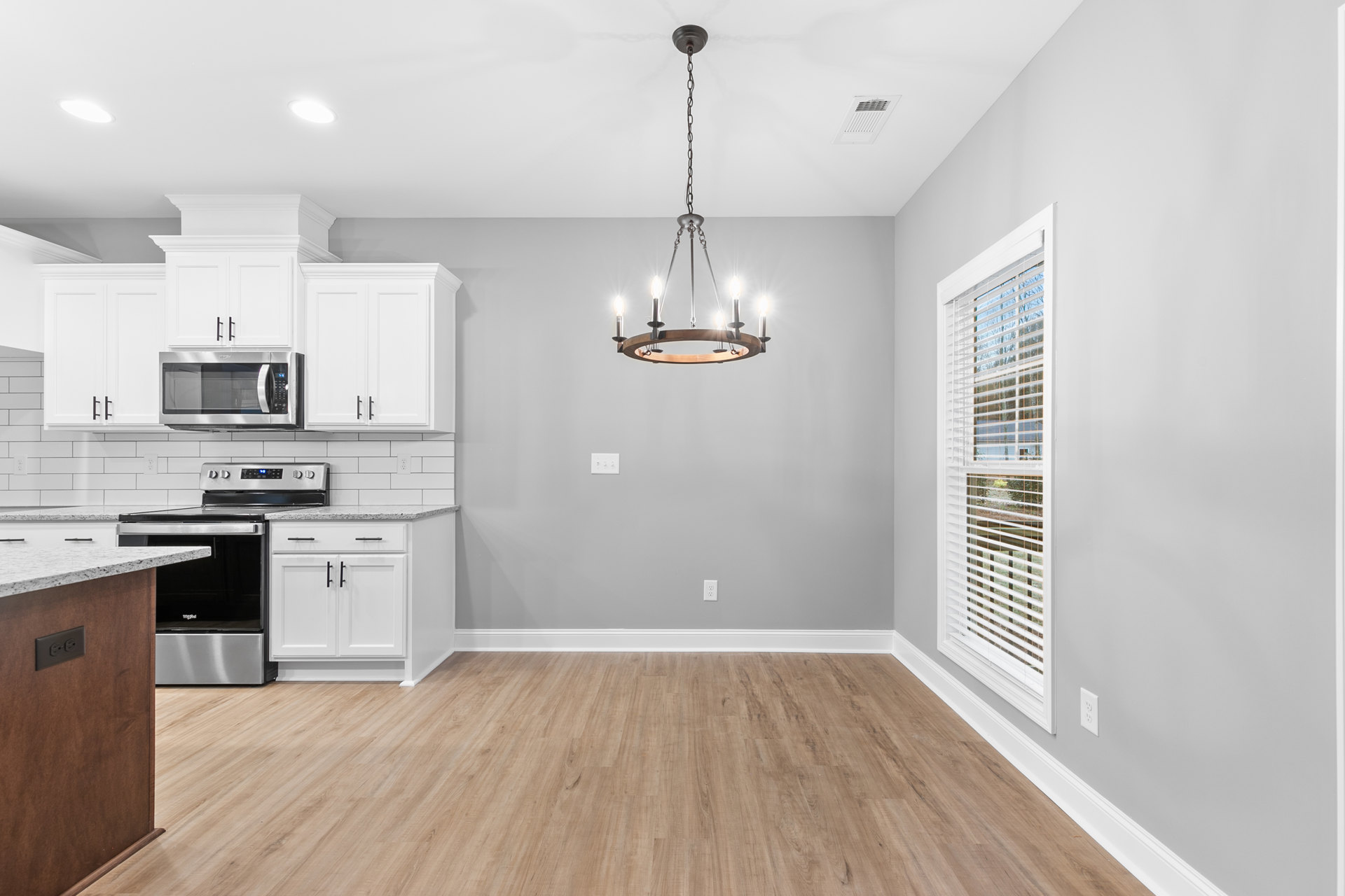 Kitchen with wood flooring, white trim, cabinetry, stove and oven, chandelier hanging from a chain, microwave, window, and countertops