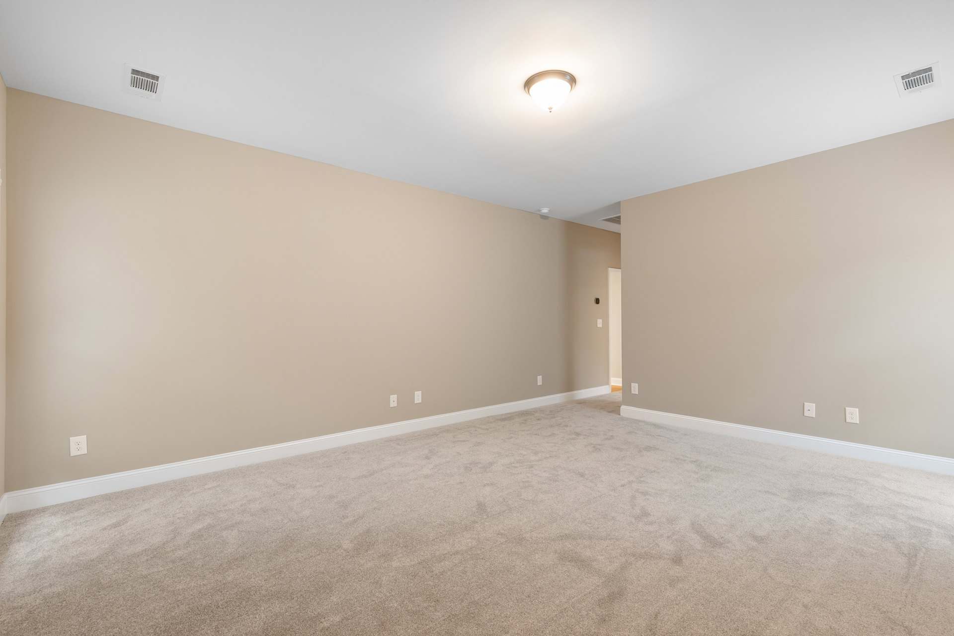 Beige walls and carpeted floor, white ceiling vent and light fixture, white trim along base of walls