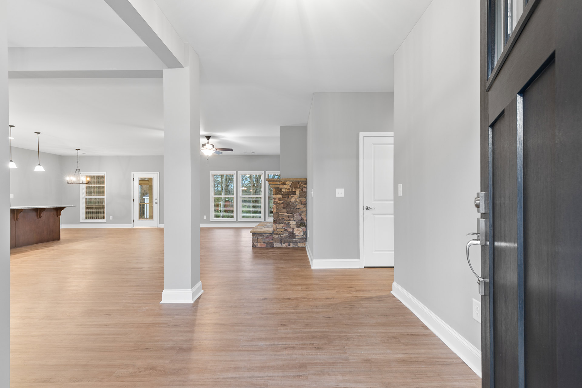 Stone fireplace with built-in bench, white door with glass window, wood flooring, ceiling fan, neutral walls