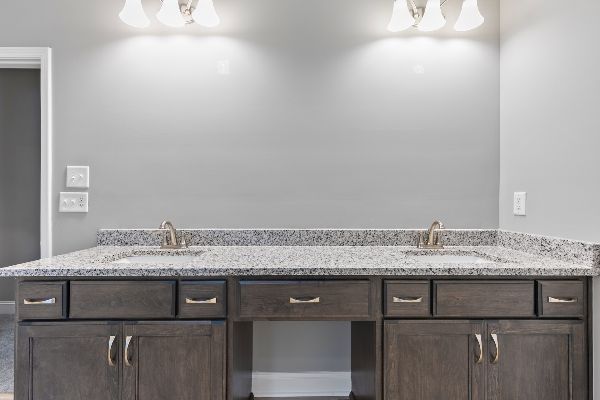 Bathroom featuring a marble countertop with dual sinks, white cabinetry with drawers, chrome faucets, light switch and wall outlet on white and grey walls, ceiling fan overhead