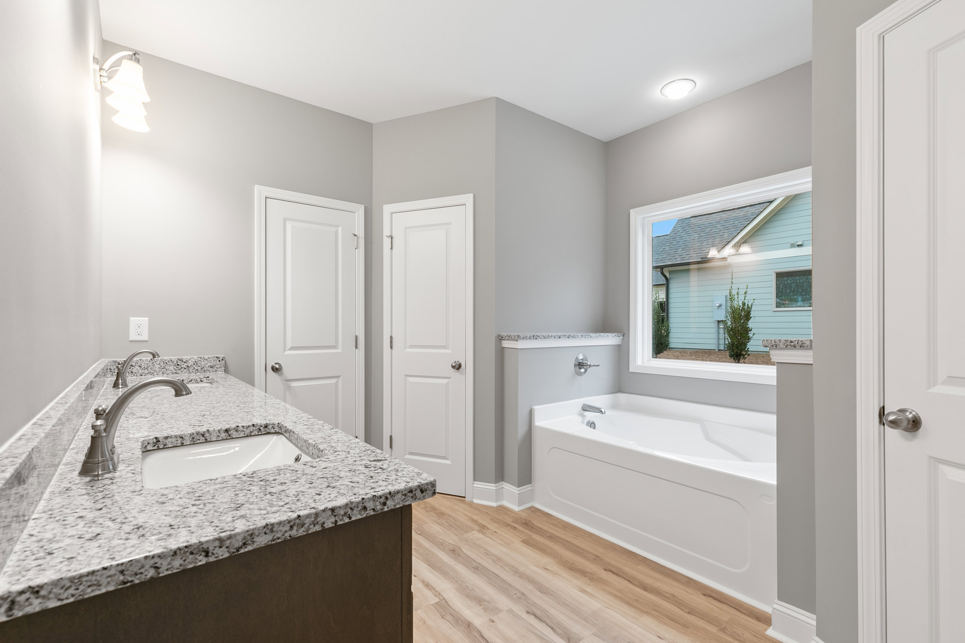 Bathroom featuring a freestanding bathtub beneath a window, white sink with black speckled countertop, silver faucet, white door with silver knob, and modern light fixture with