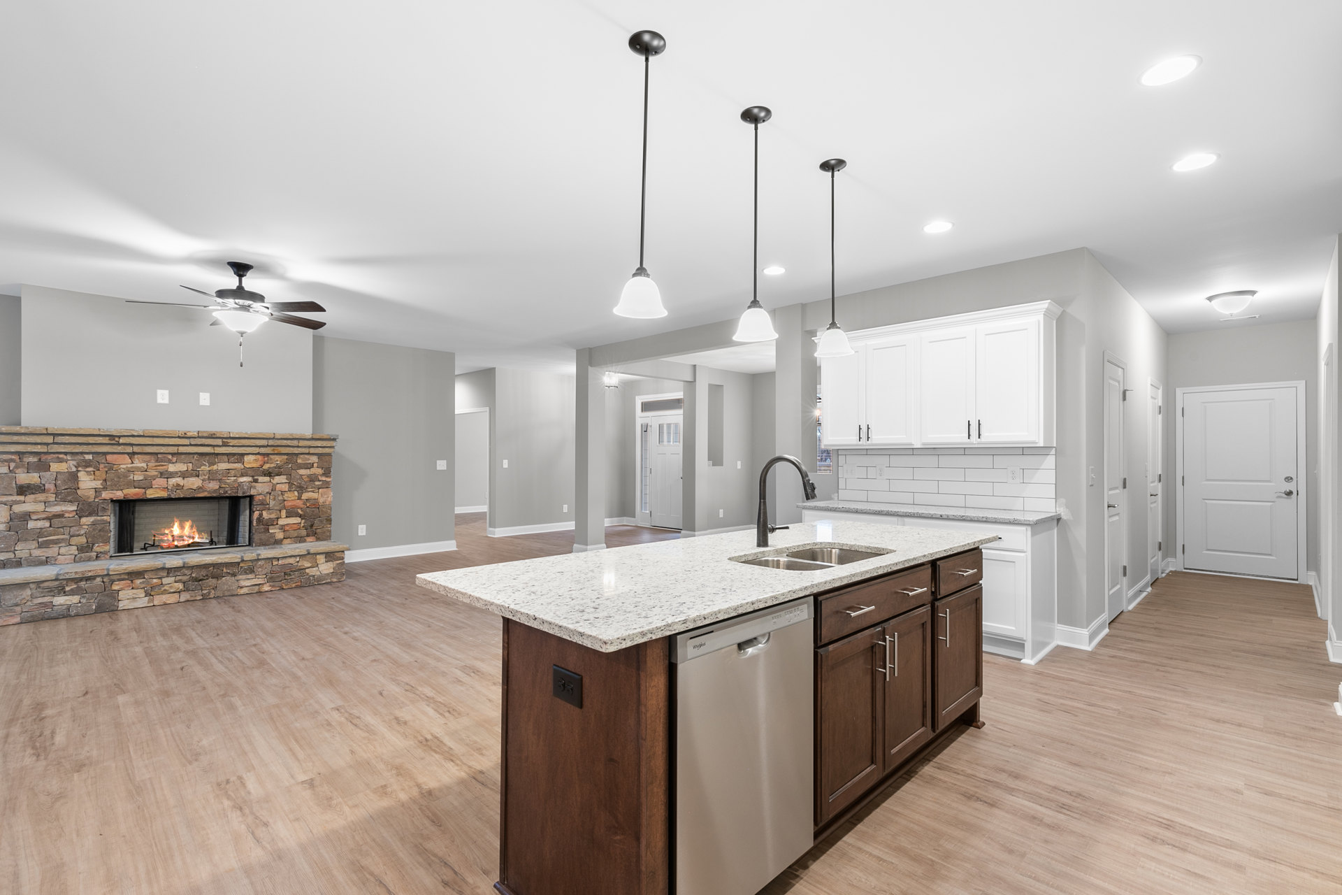 Kitchen featuring a stone fireplace with active fire, expansive central island with light countertop, white cabinetry, stainless steel sink, tiled floor, and white door with silver