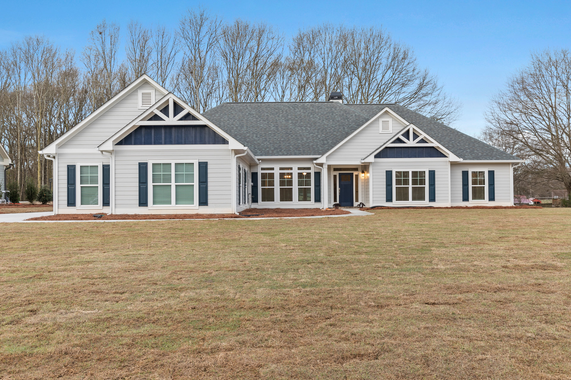 Two-story house with white siding, blue front door, manicured lawn, mature trees in background, large windows with white frames and blinds