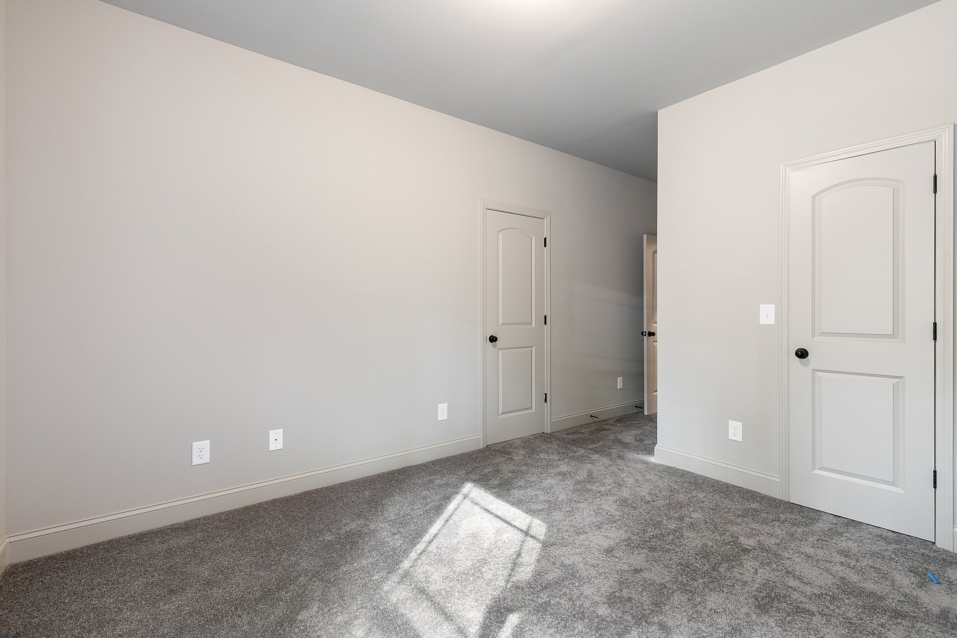 White walls and grey carpeted floor, white door with black knob, ceiling light casting illumination onto carpet