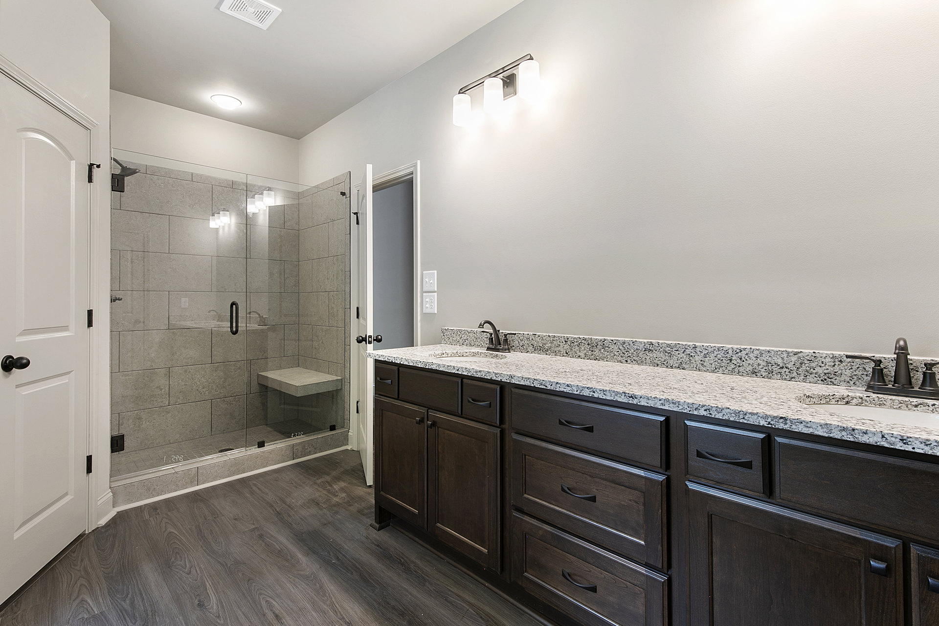 Bathroom with glass shower enclosure, white vanity with undermount sink, chrome faucet, light gray tile flooring, and white paneled door with black hardware