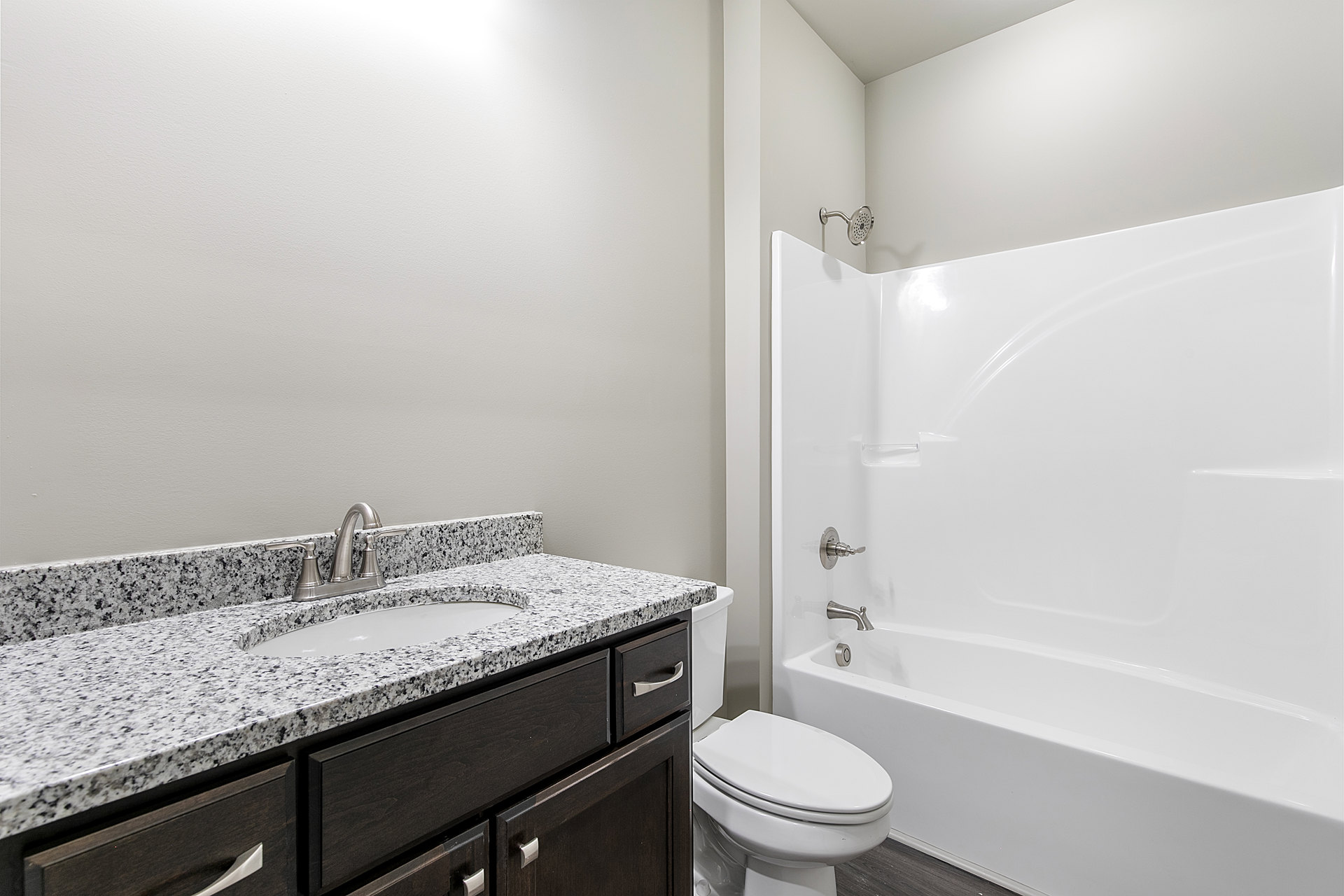Bathroom with white tile walls, built-in shower, white bathtub, closed toilet, modern sink with chrome faucet, and wood cabinetry under quartz countertop