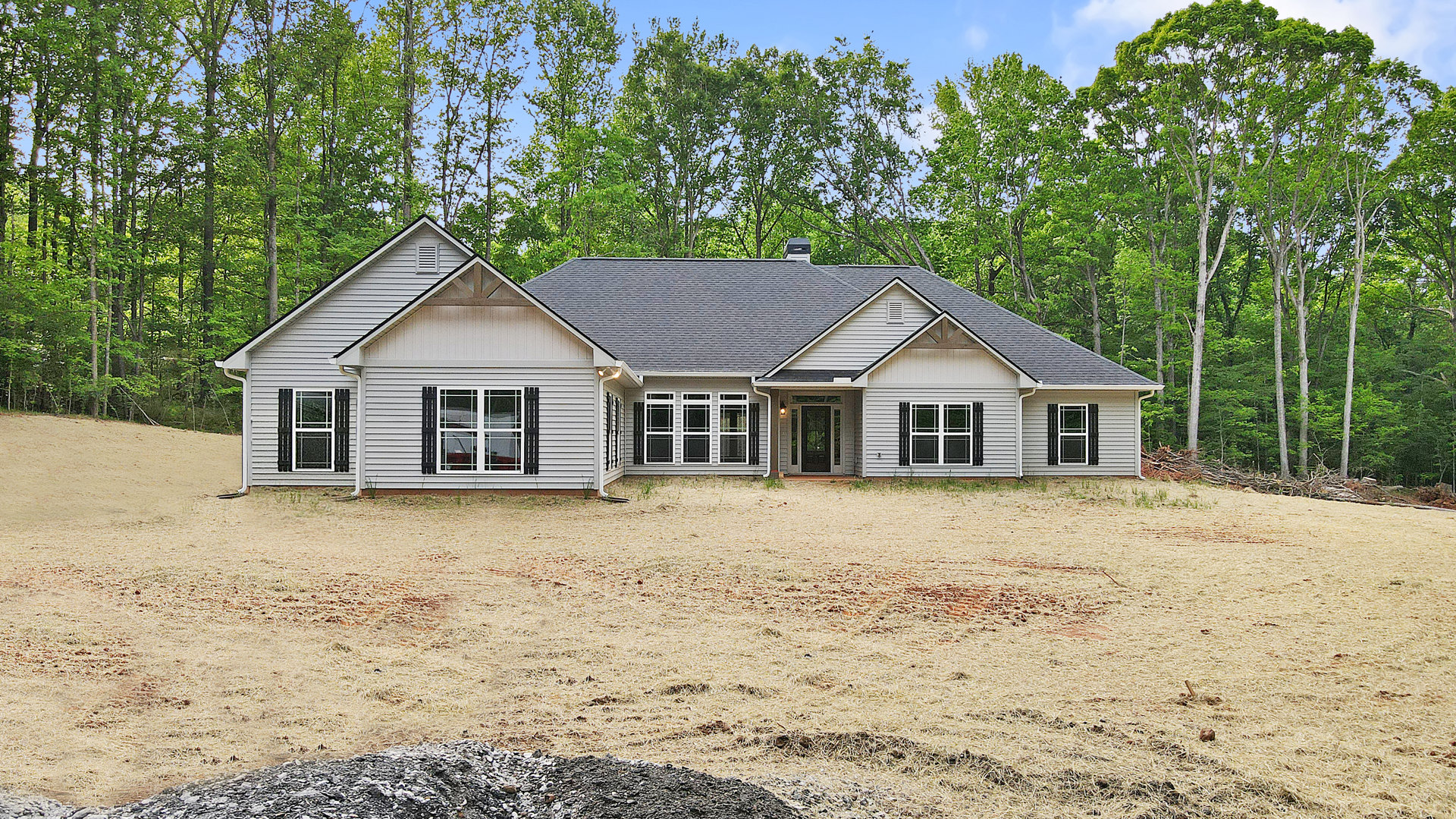 Two-story house with white-framed windows, black front door with side light, surrounded by trees and a large grassy yard