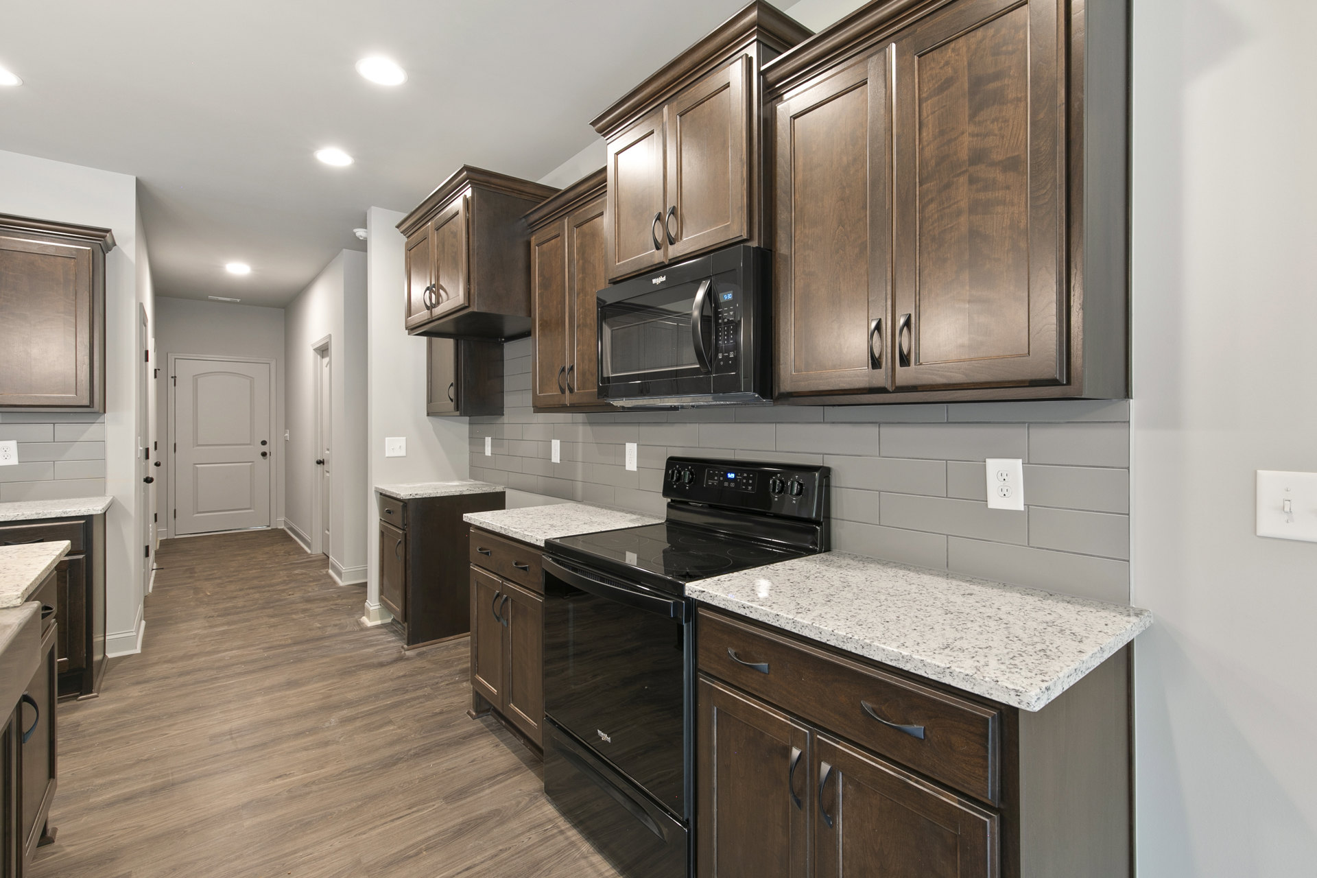 Dark wood kitchen cabinets, black microwave oven, black stove, white door with black handles, electrical outlet, wood door detail, light countertops
