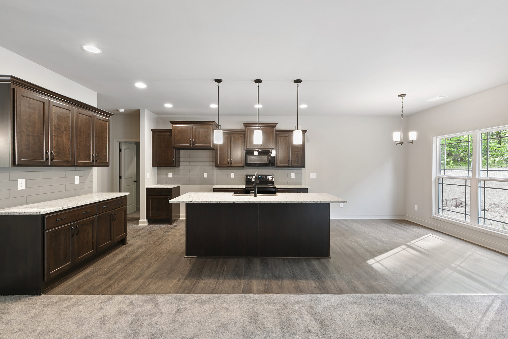 Spacious kitchen featuring a large marble island with built-in sink, black stove, white cabinetry, and a window overlooking a forest