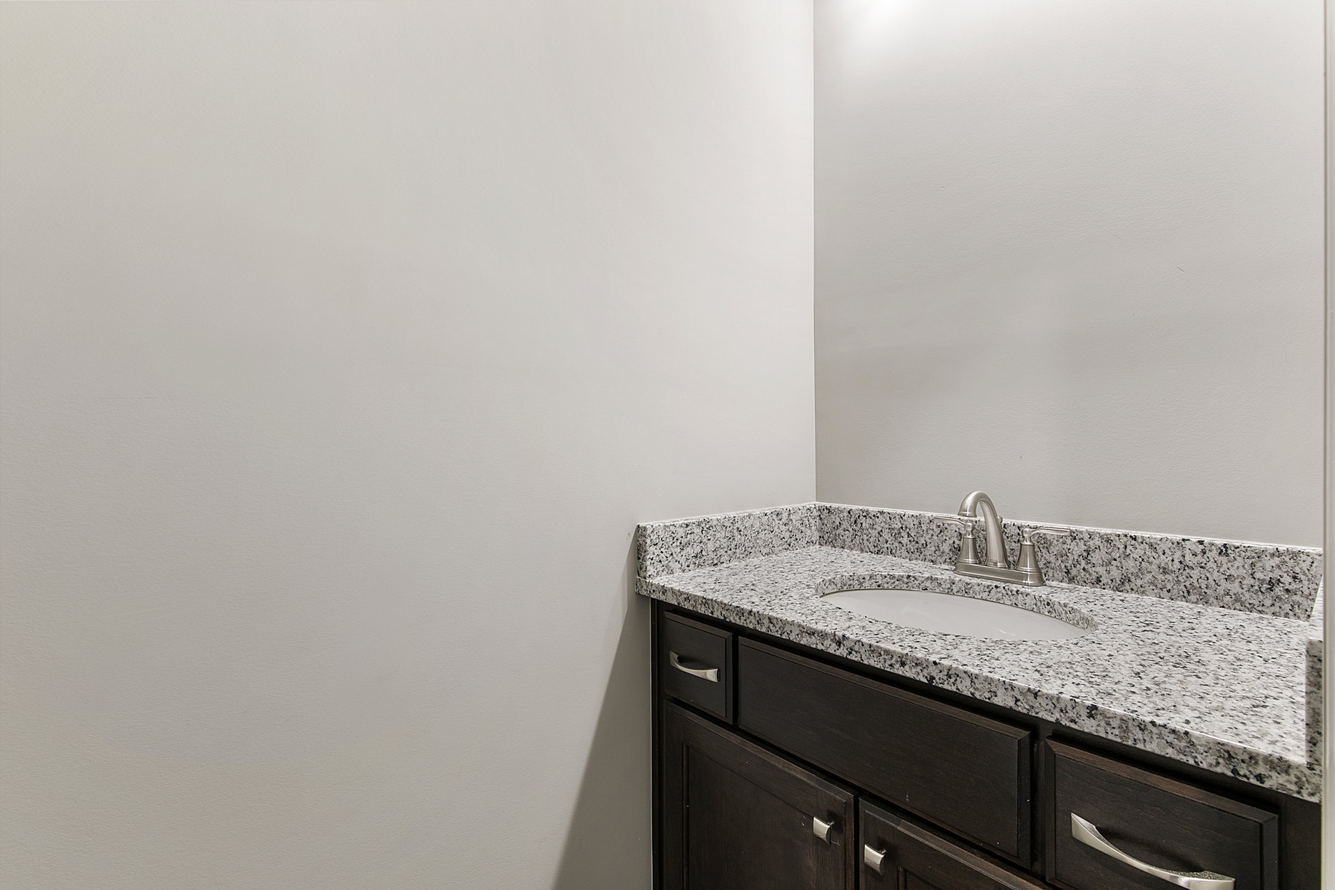 White undermount sink set in a speckled granite countertop with chrome faucet, surrounded by light wood cabinetry and drawers