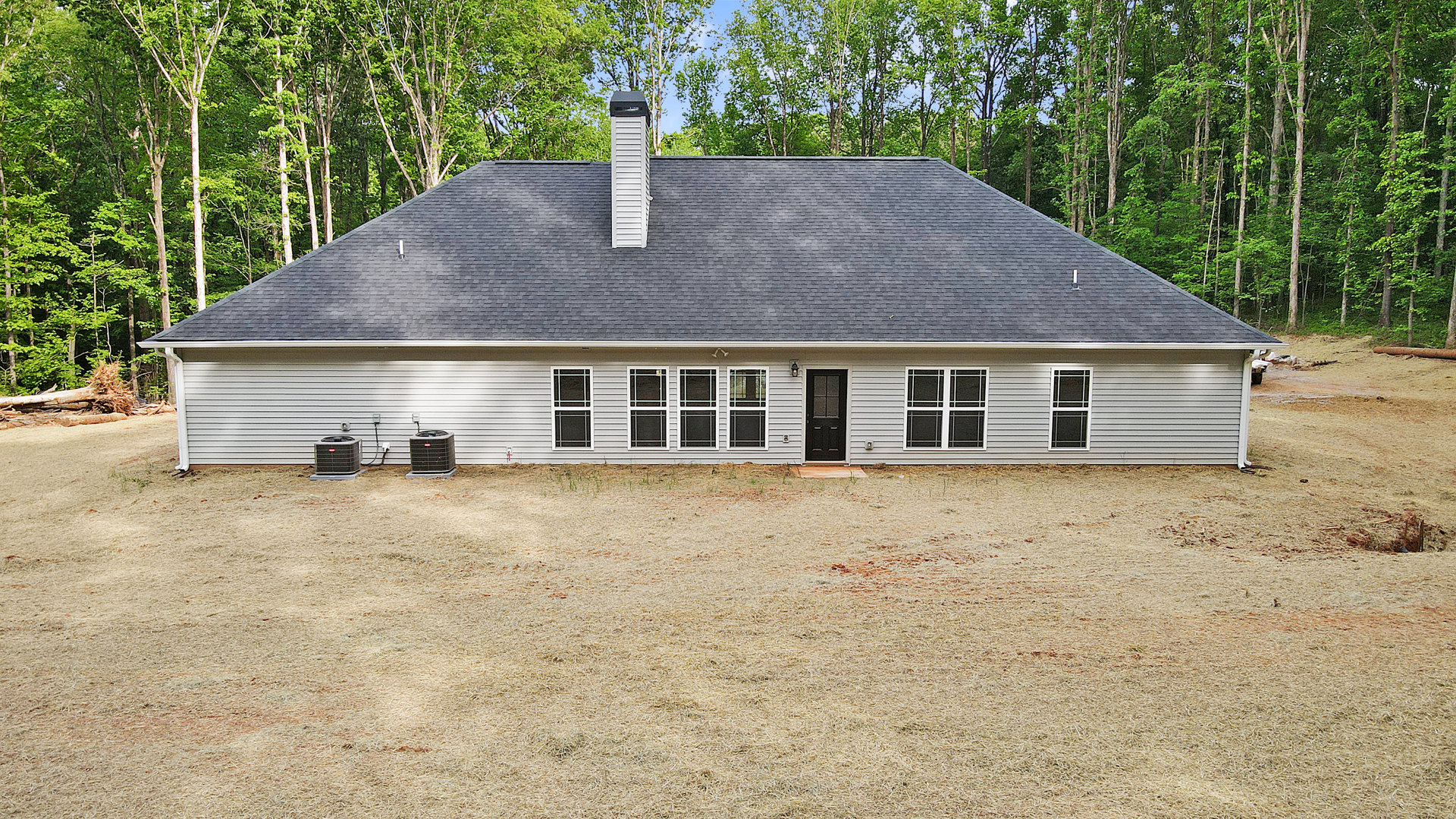 White cottage-style house with black-framed windows, black glass-paneled front door, brick chimney, grassy backyard, and outdoor heat pump unit.