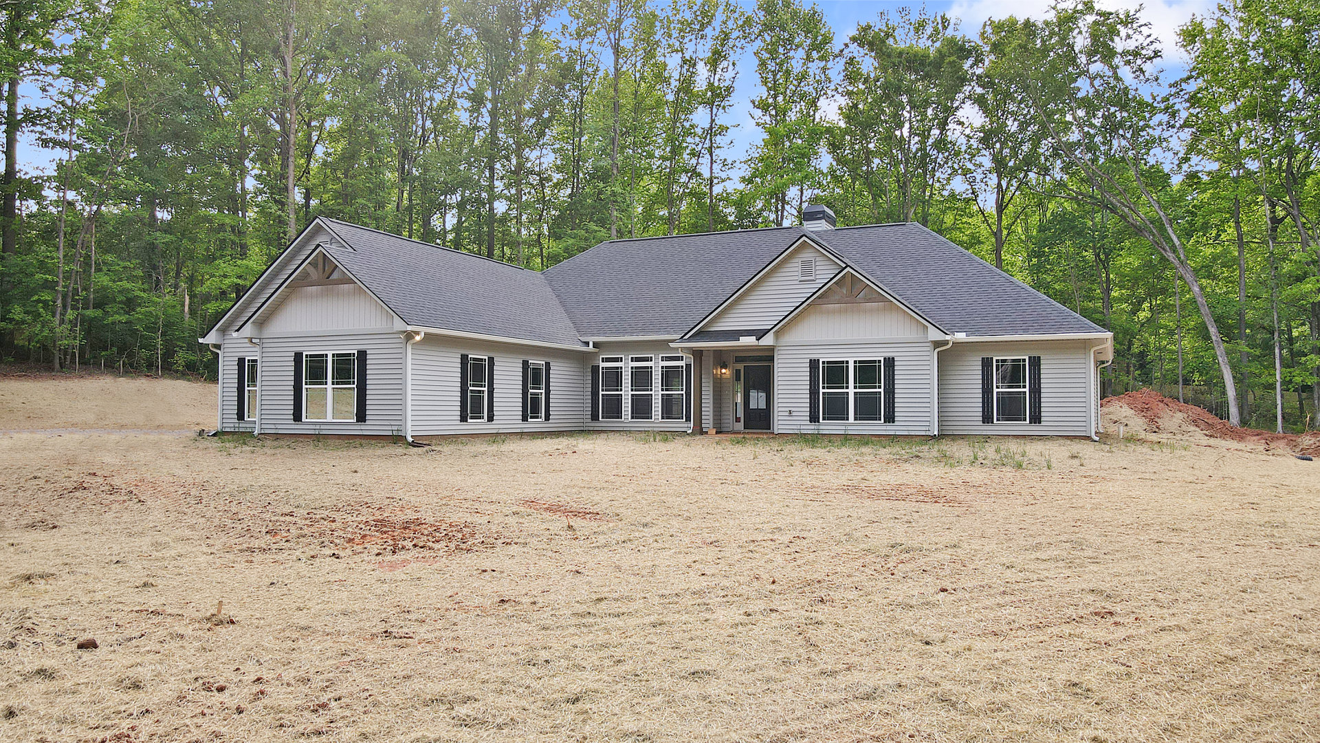 Two-story custom home with black and white framed windows, surrounded by mature trees and a spacious grassy yard