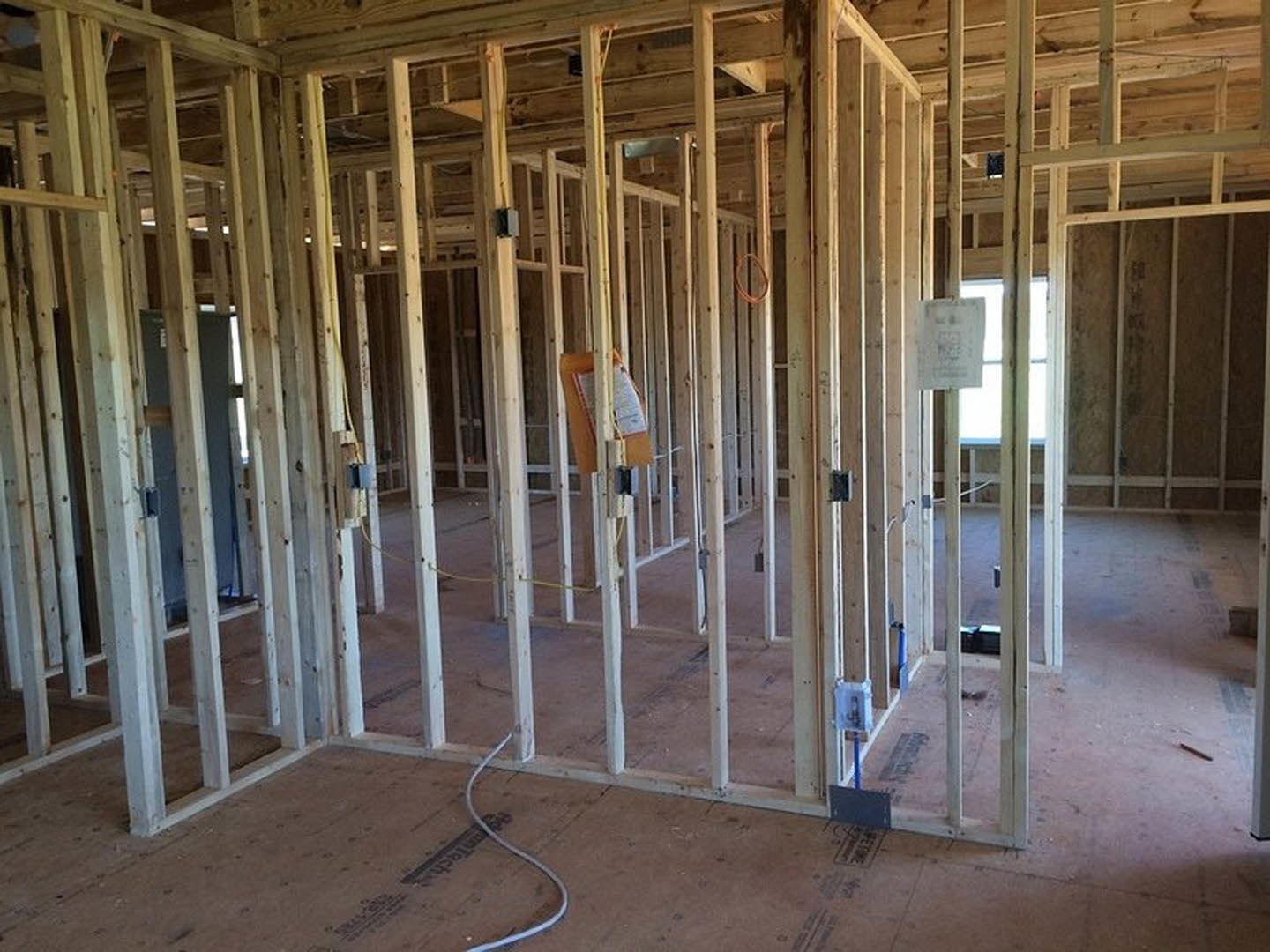 Exposed wooden ceiling beams, unfinished drywall, and insulation in a residential home under construction
