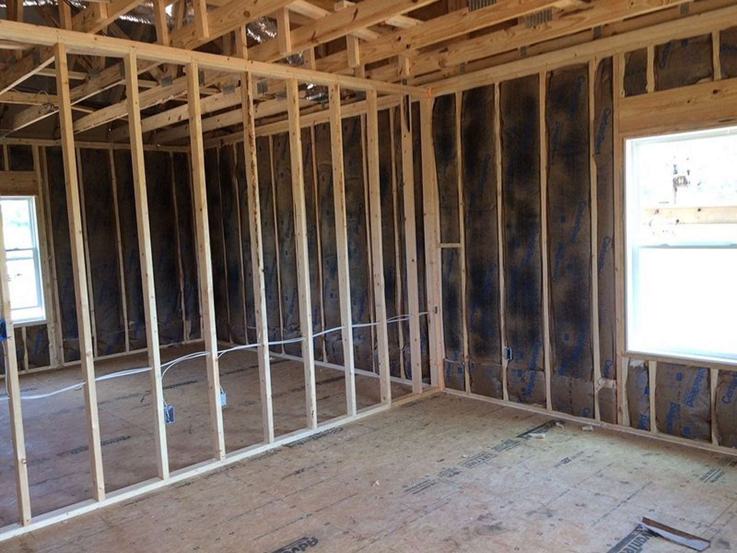 Wood-framed room under construction with exposed beams, unfinished walls, and a large window letting in natural light