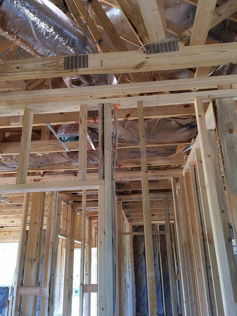 Exposed wood framing with metal brackets, white wall illuminated by overhead light, pile of insulation material on wooden shelf, close-up of metal foil, wooden ladder with metal