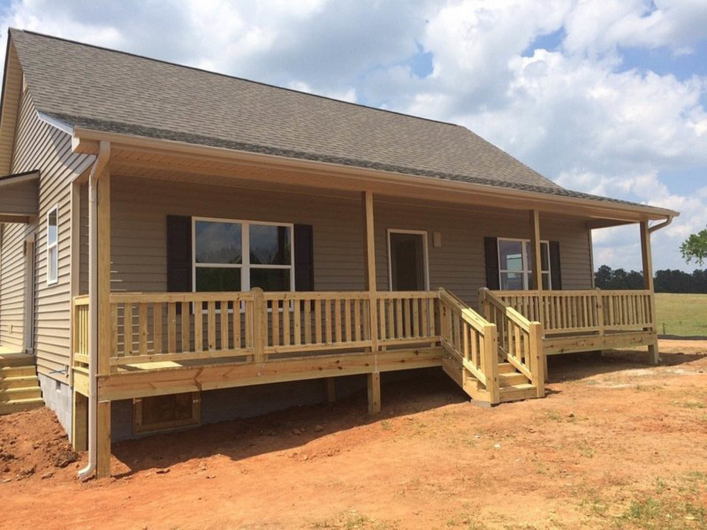 Two-story home with gray siding, white-trimmed windows, covered porch featuring wooden deck and stairs, fenced railing, cloudy sky overhead, tree partially visible in foreground