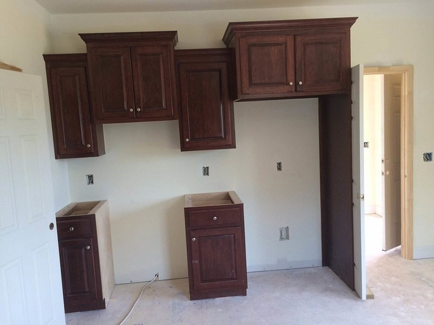 Dark wood kitchen cabinets with silver handles, white door with doorknob and side light, light-colored countertop, hardwood flooring