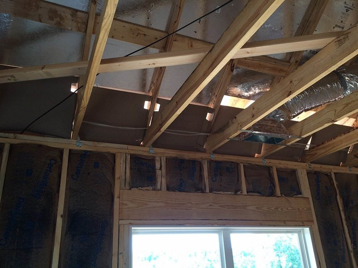 Exposed wooden beams and framing with a white-framed window, metal roof, and unfinished interior walls