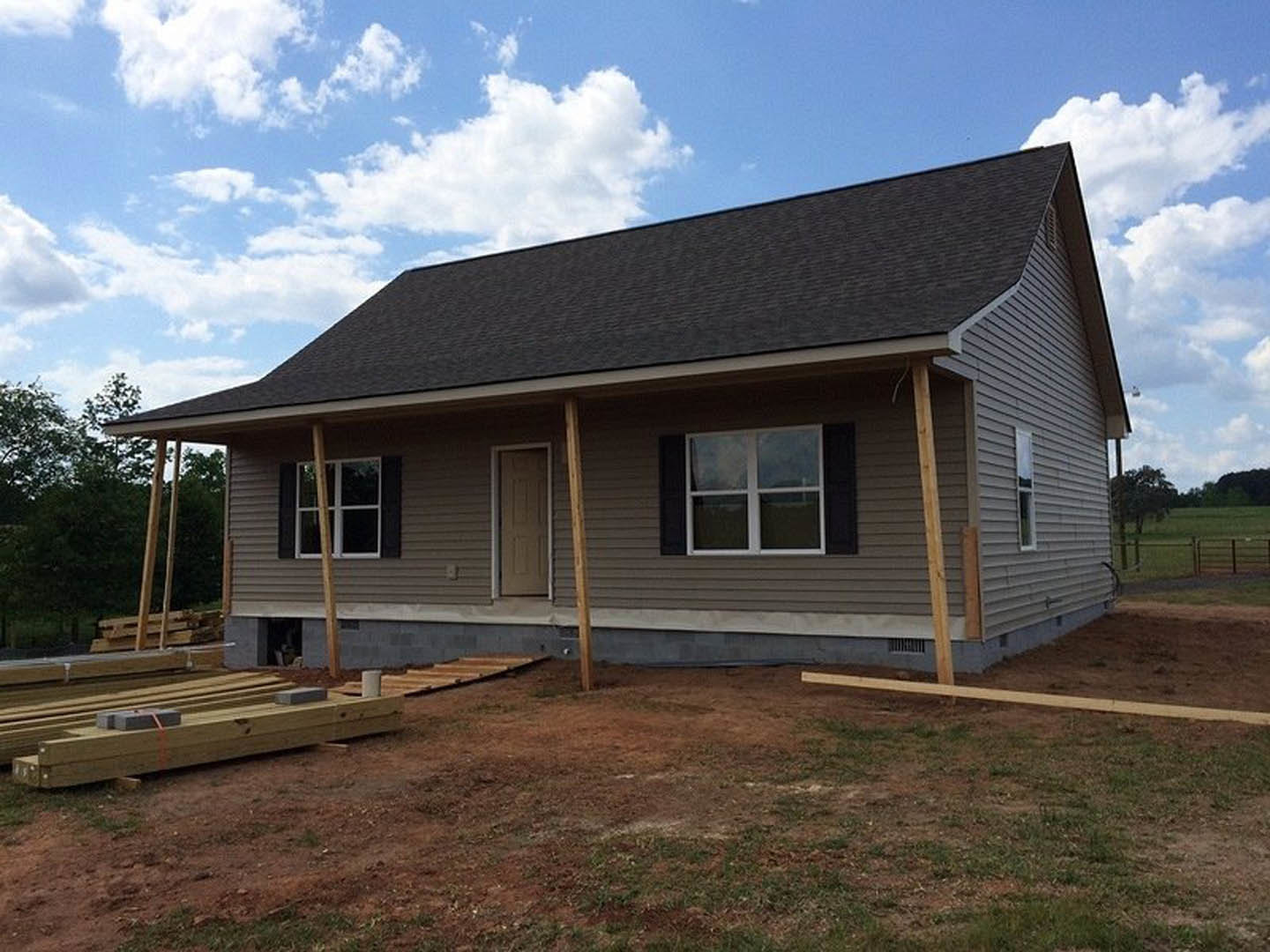 Framed house under construction with exposed wood beams, white door and window, dirt lot, and blue sky in background