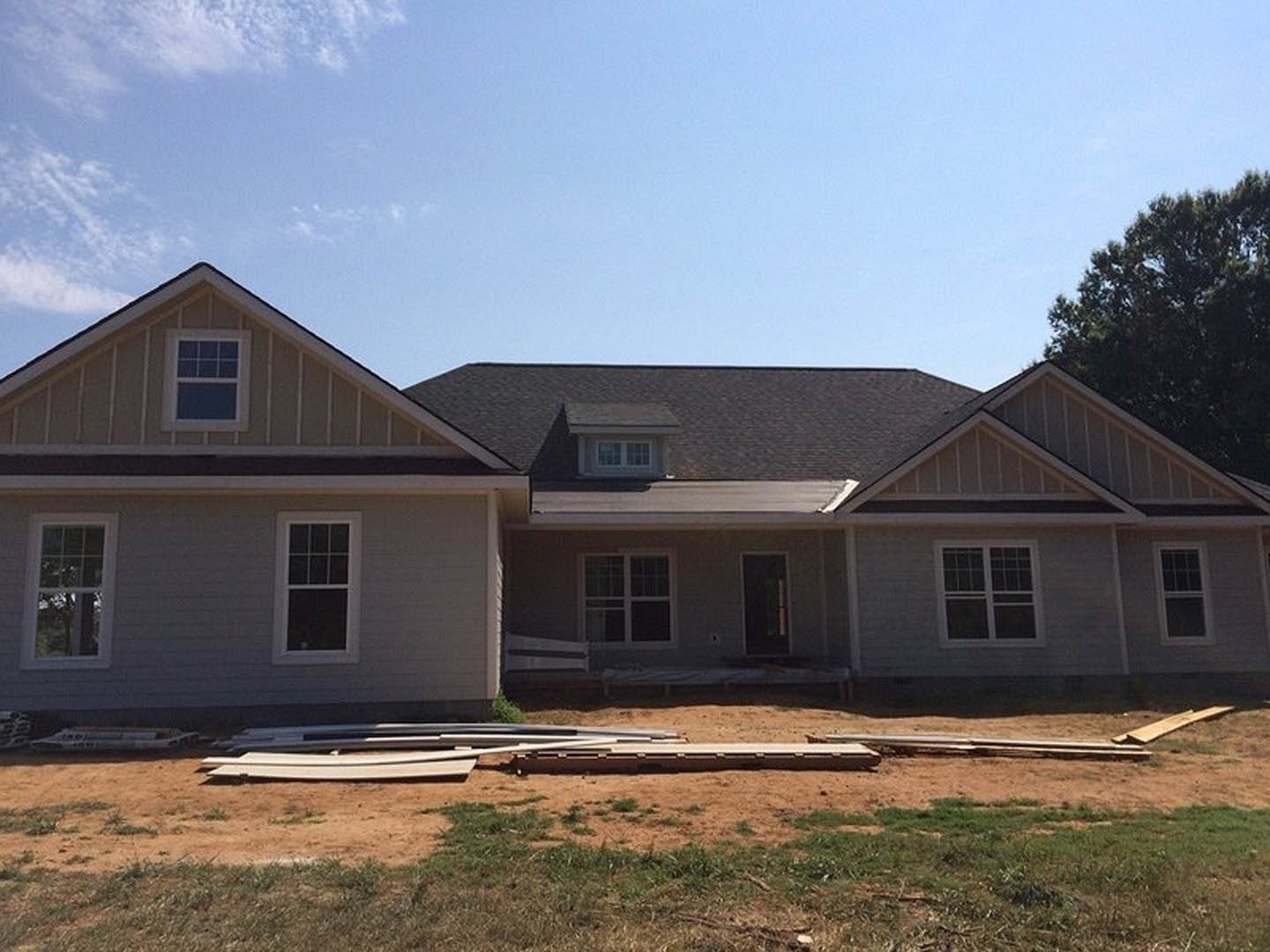 Partially built house with exposed wooden framing, white square window, unfinished siding, and roof under clear blue sky