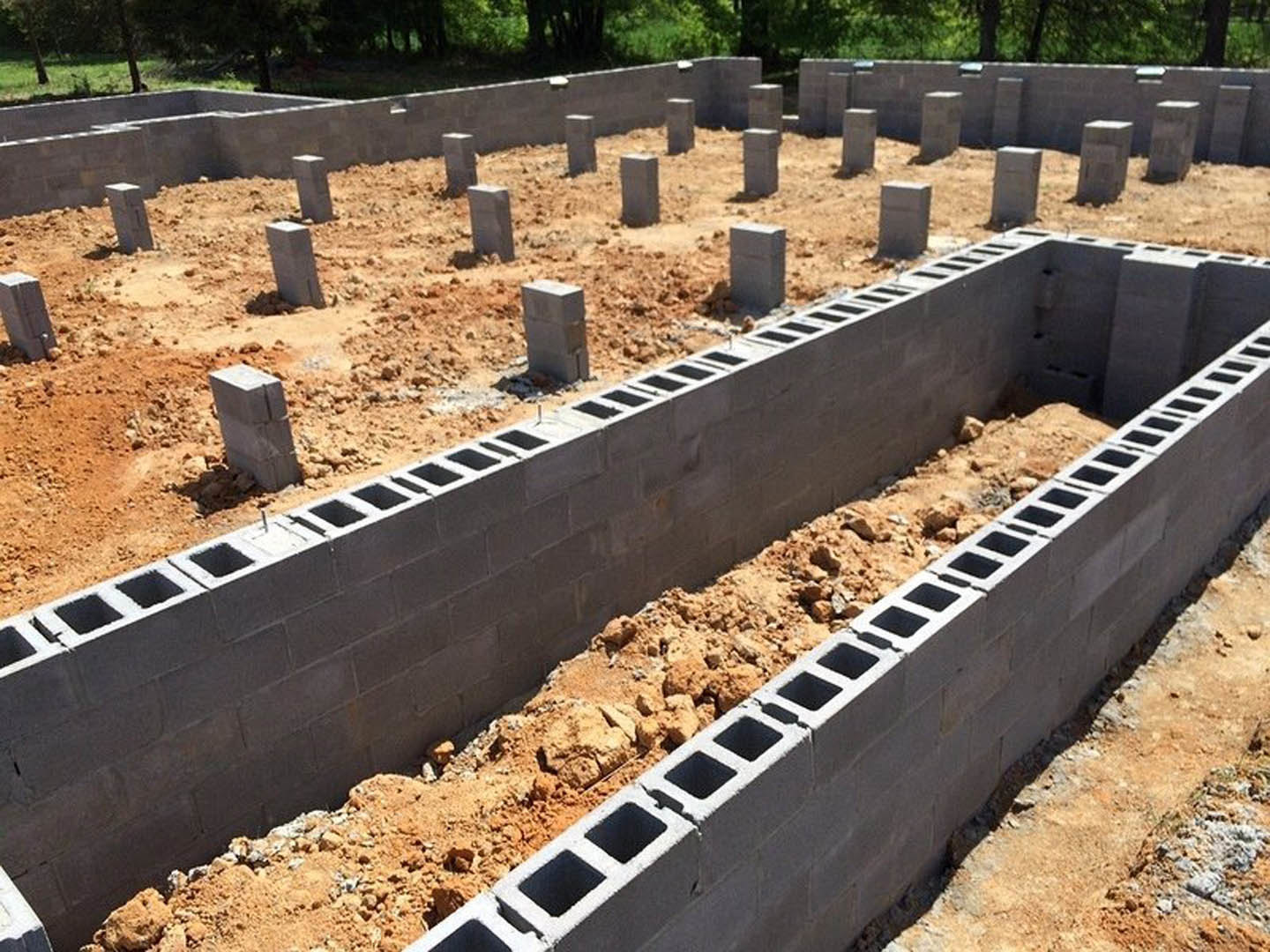 Concrete foundation with stacked concrete blocks on a construction site, surrounded by dirt and sparse vegetation.