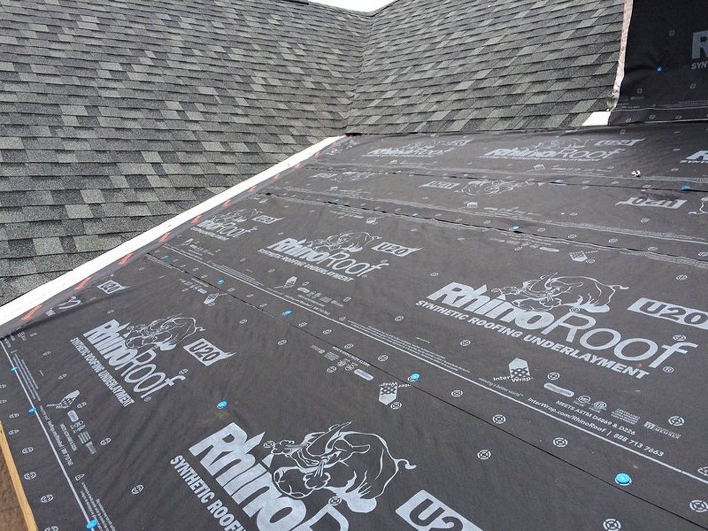 Black tarp covering roof with white circular logo and text, surrounded by grey roofing material